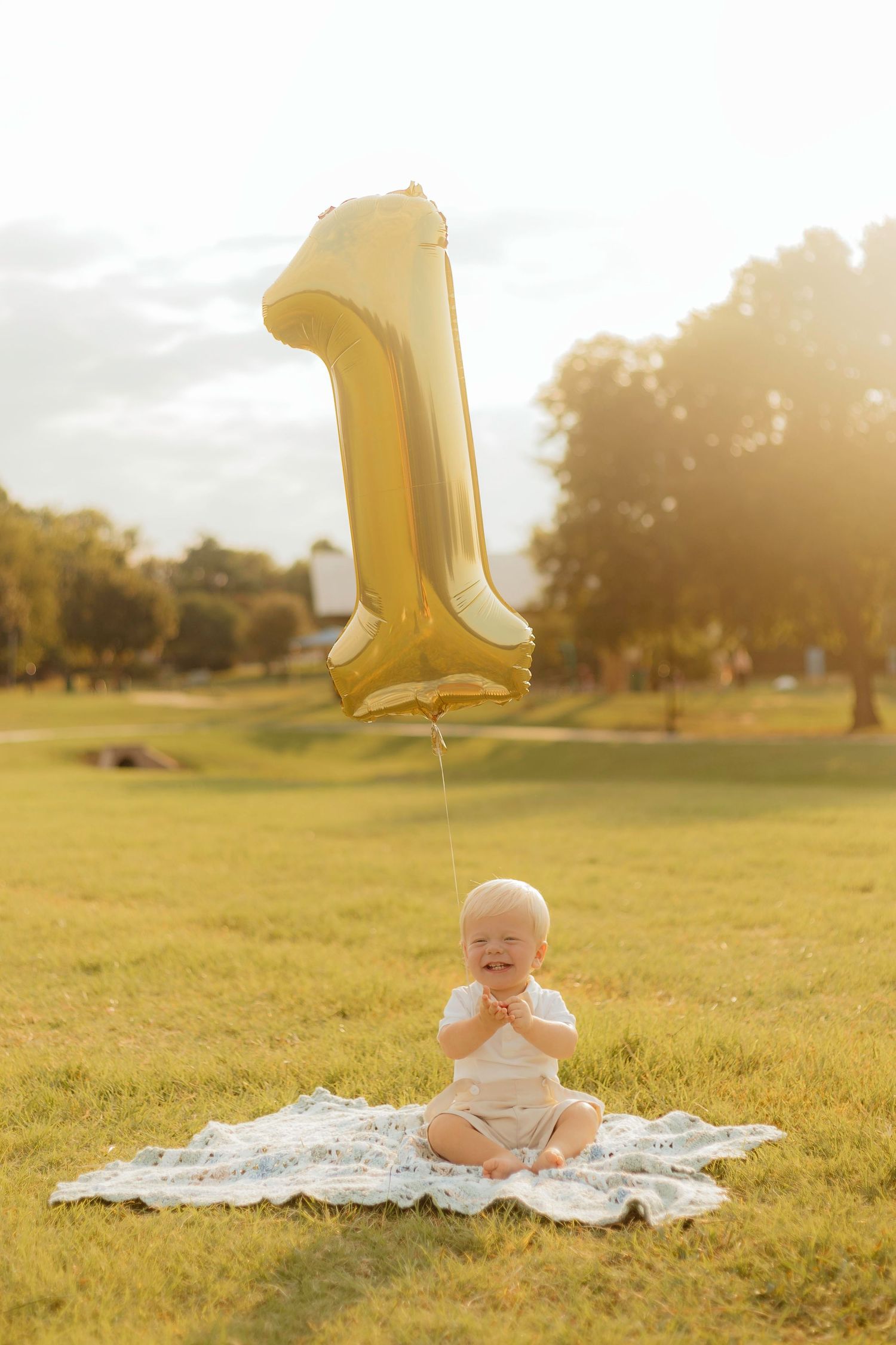 A gold number one balloon floats against a sunlit grassy field with a white blanket.
