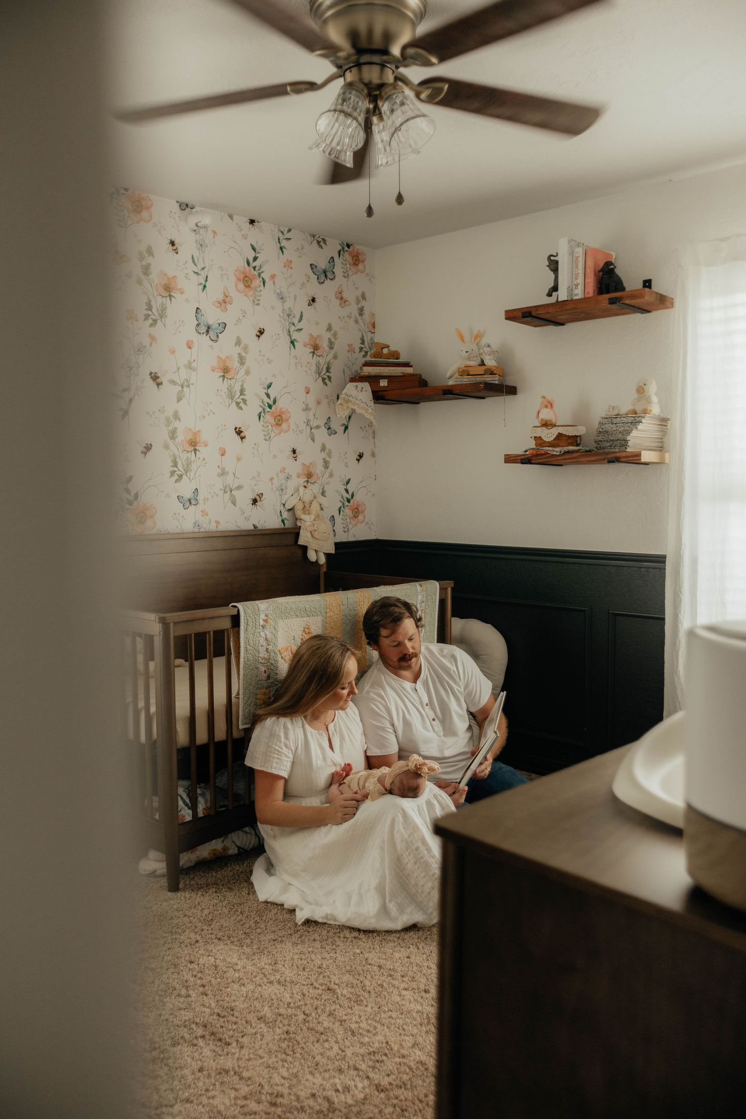 Couple relaxing together on floor of room with floral wallpaper and ceiling fan.