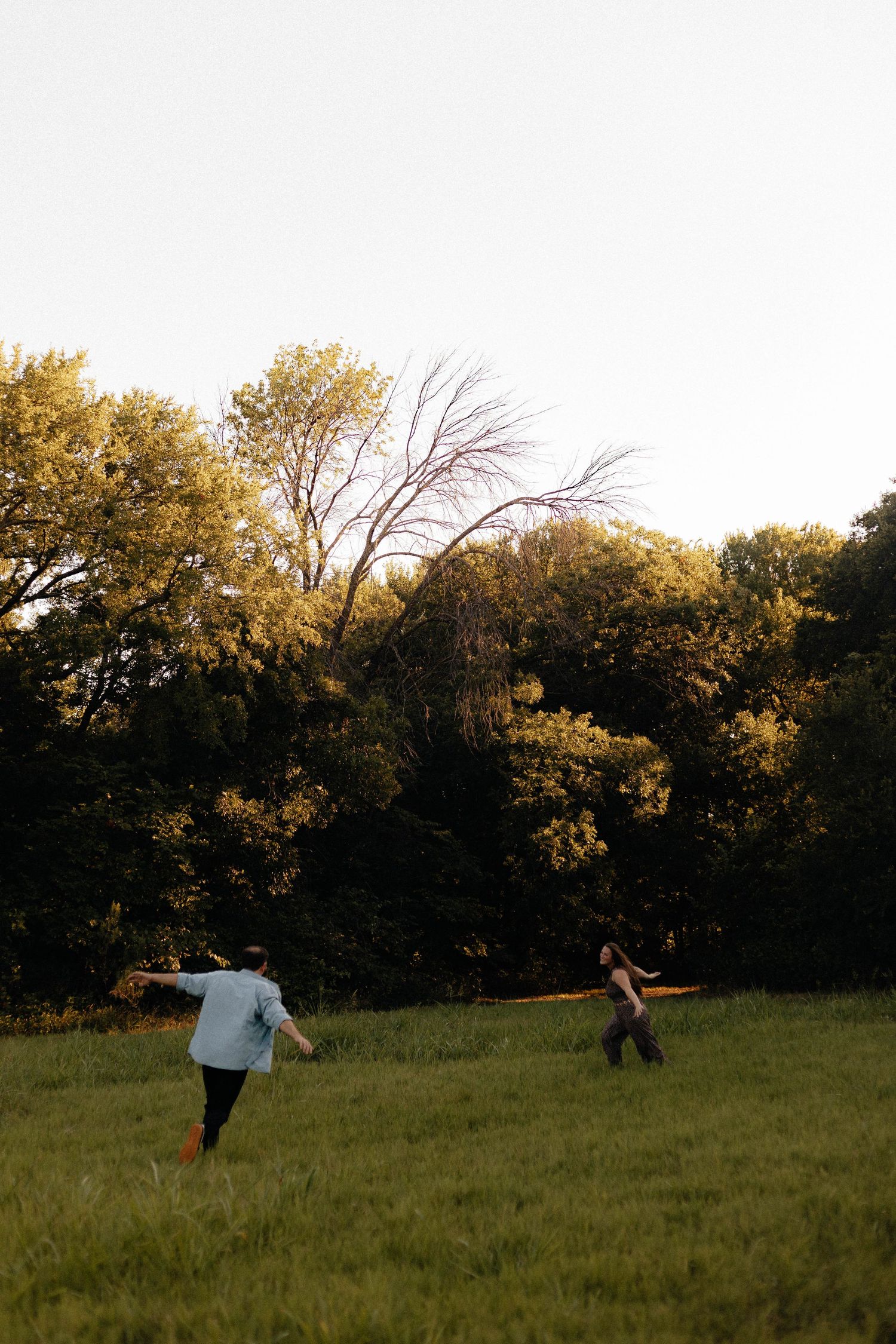 People playfully run and jump in a grassy field at golden hour.