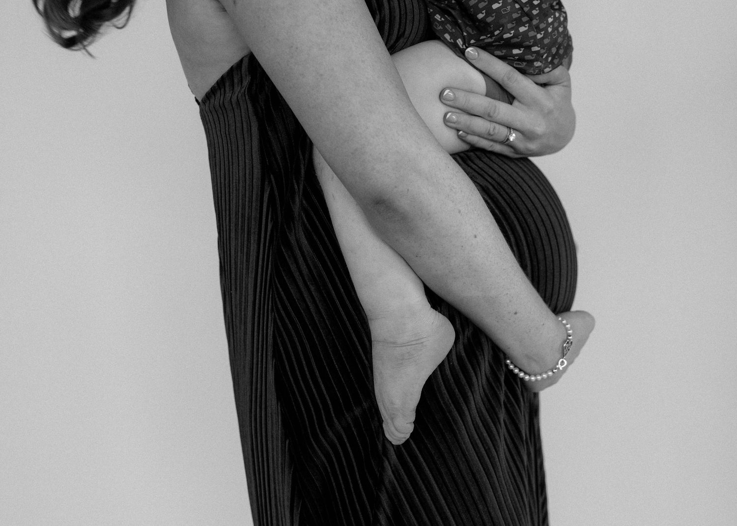 Black and white photo of a pregnant woman in striped dress holding a baby against her baby bump.