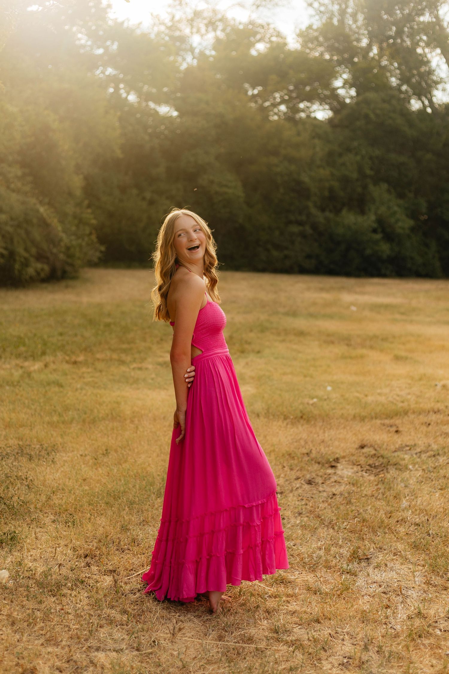 Person in bright pink flowing dress twirling in golden sunlit field.