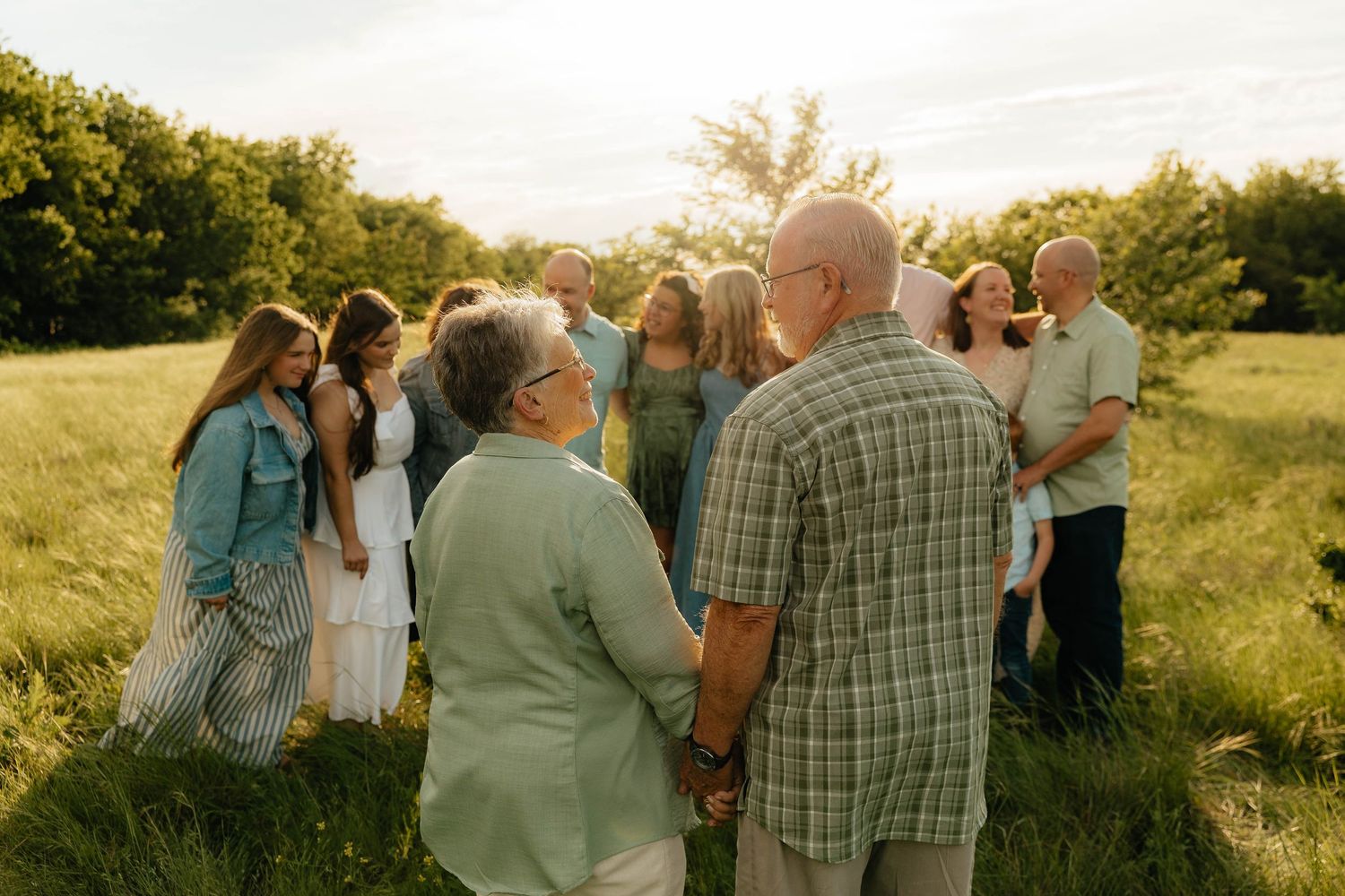Family group holding hands in a circle in a sunny green meadow during golden hour outdoor photography.