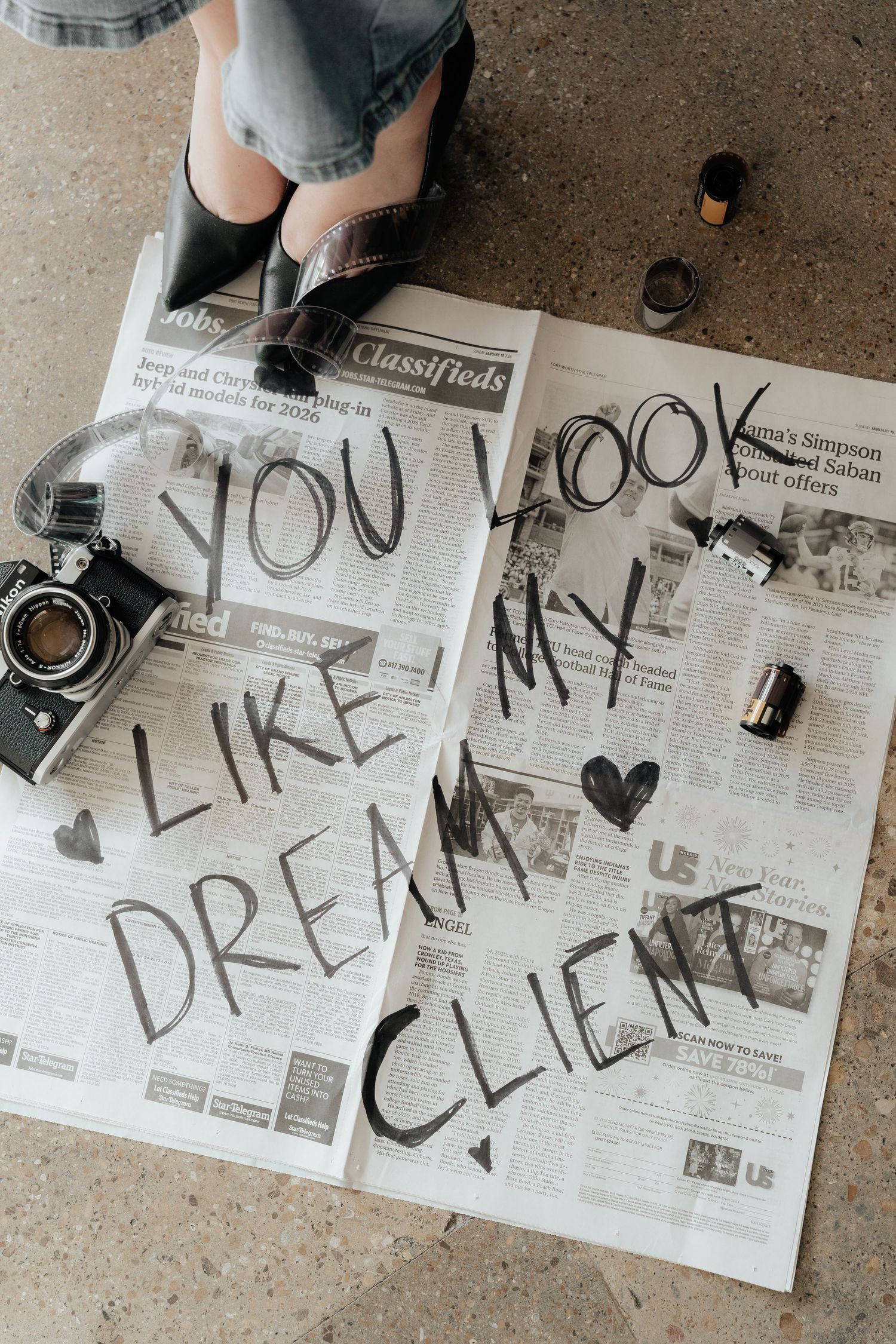 Black text spelling 'Like you dream clean' written across newspaper pages laid out on concrete floor.