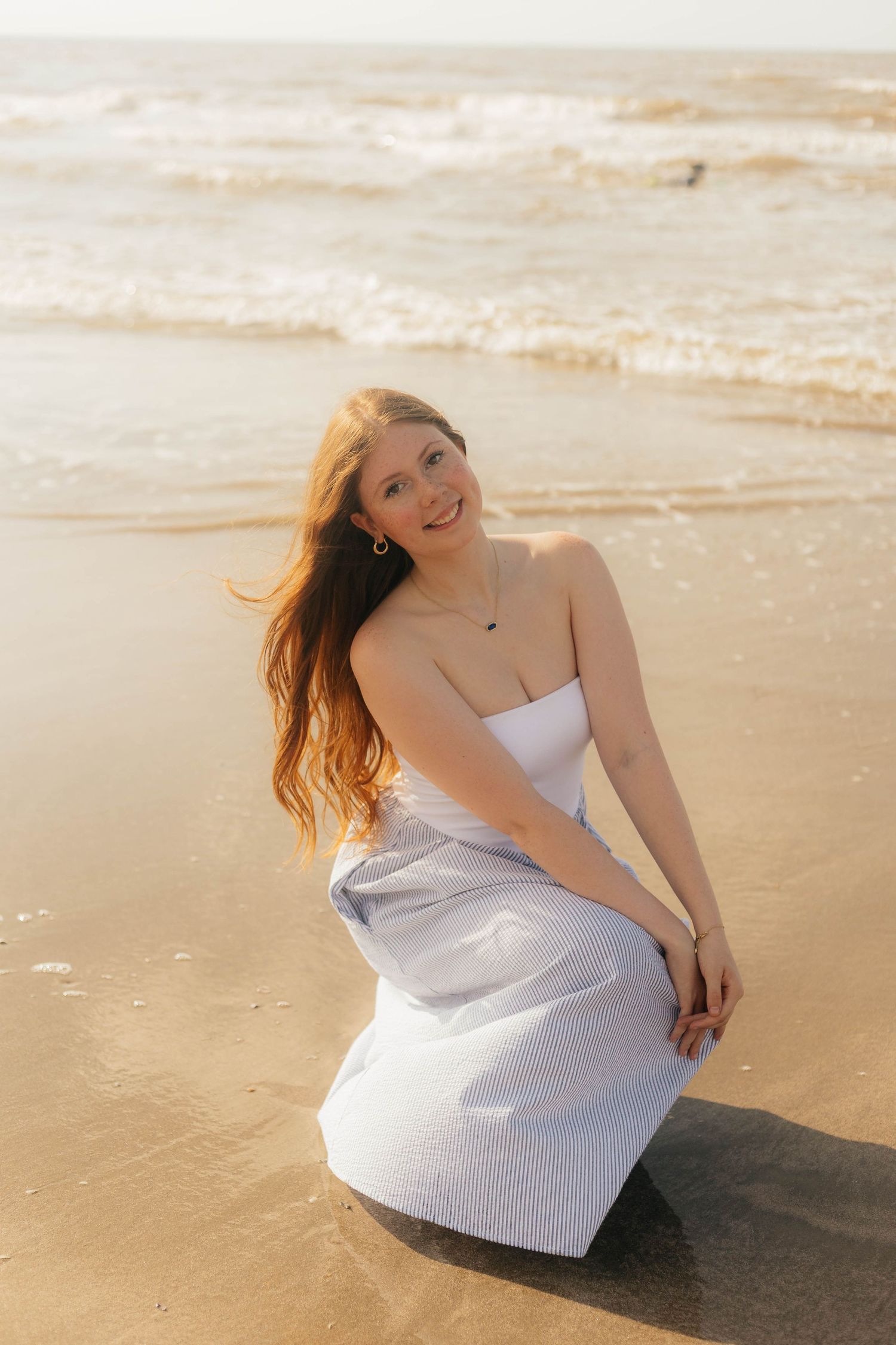 Woman in white dress posing playfully on sandy beach at sunset.