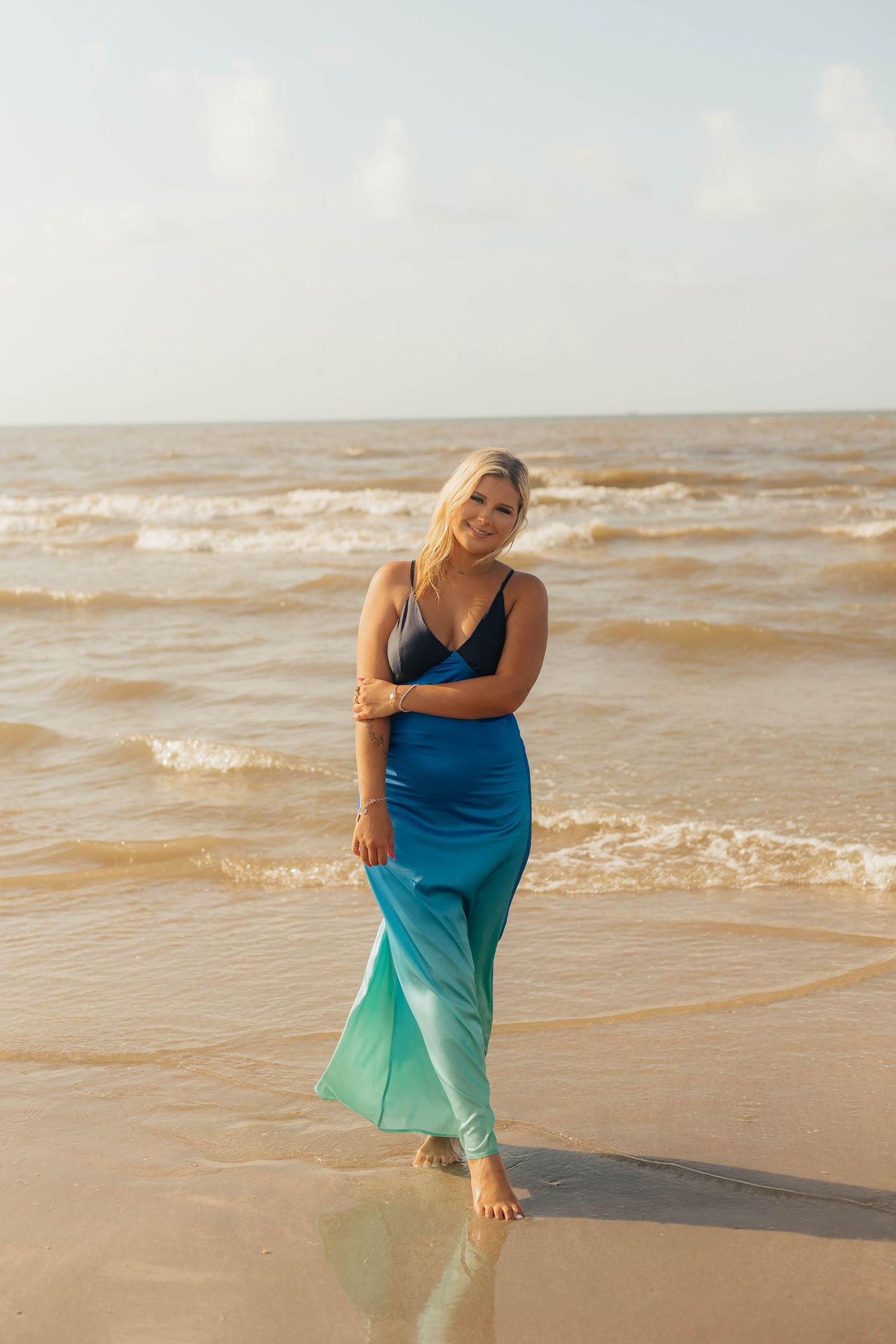 Woman in blue ombre dress posing at the beach during golden hour.