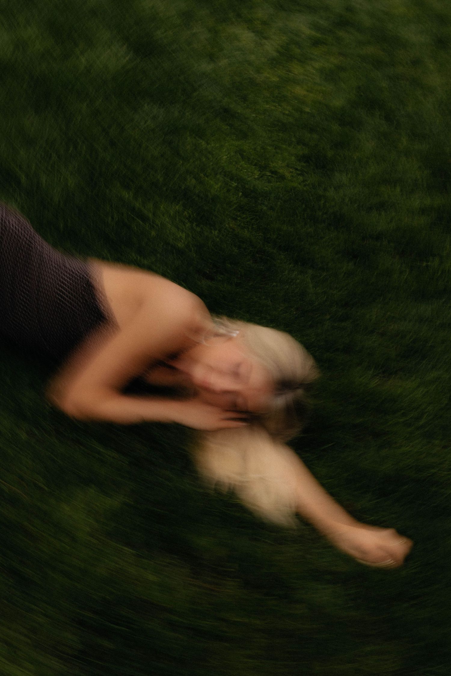 Blurred motion photo of a woman with blonde hair lying on lush green grass, captured from above.