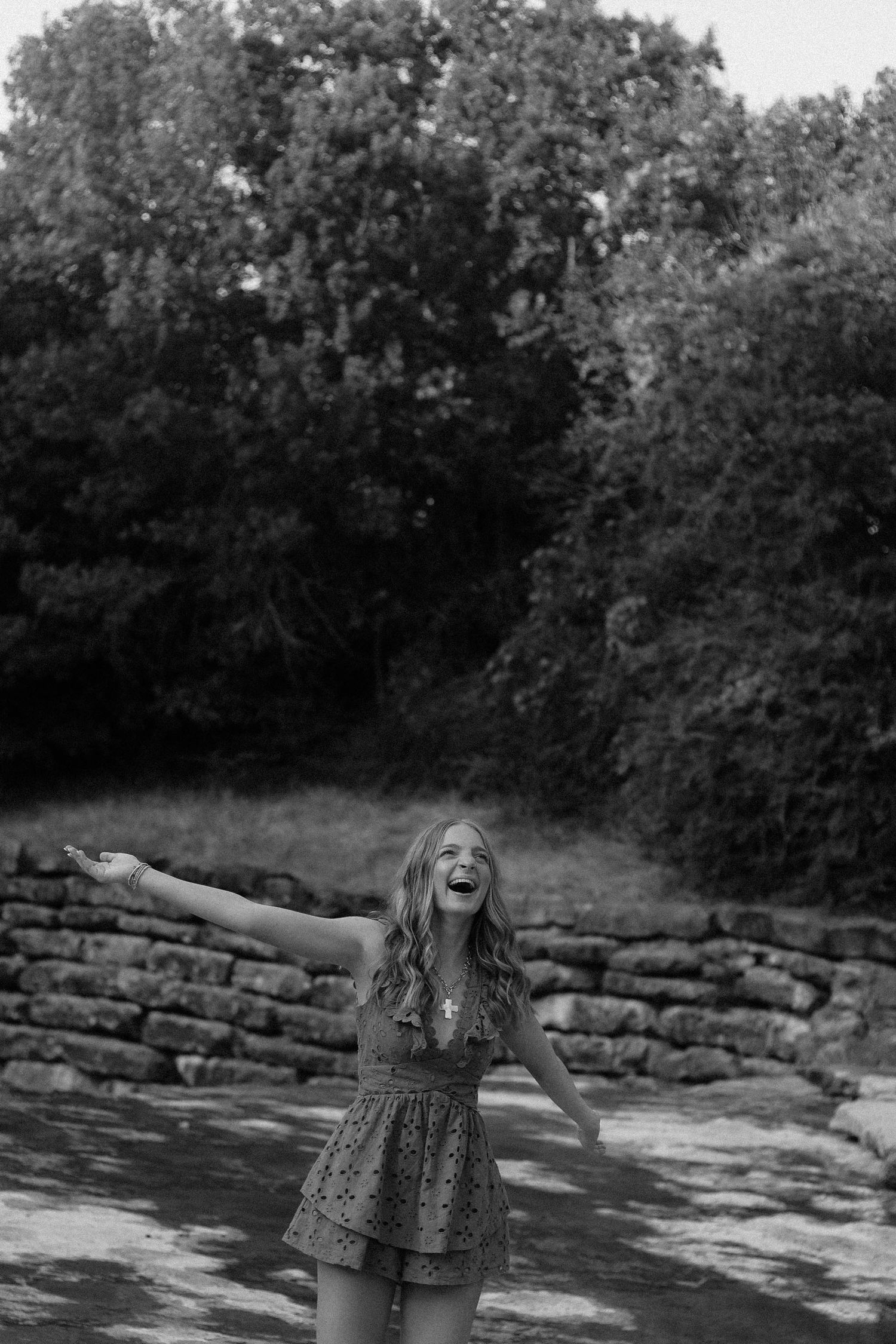 Person in patterned dress posing expressively by stone wall in black and white photograph.