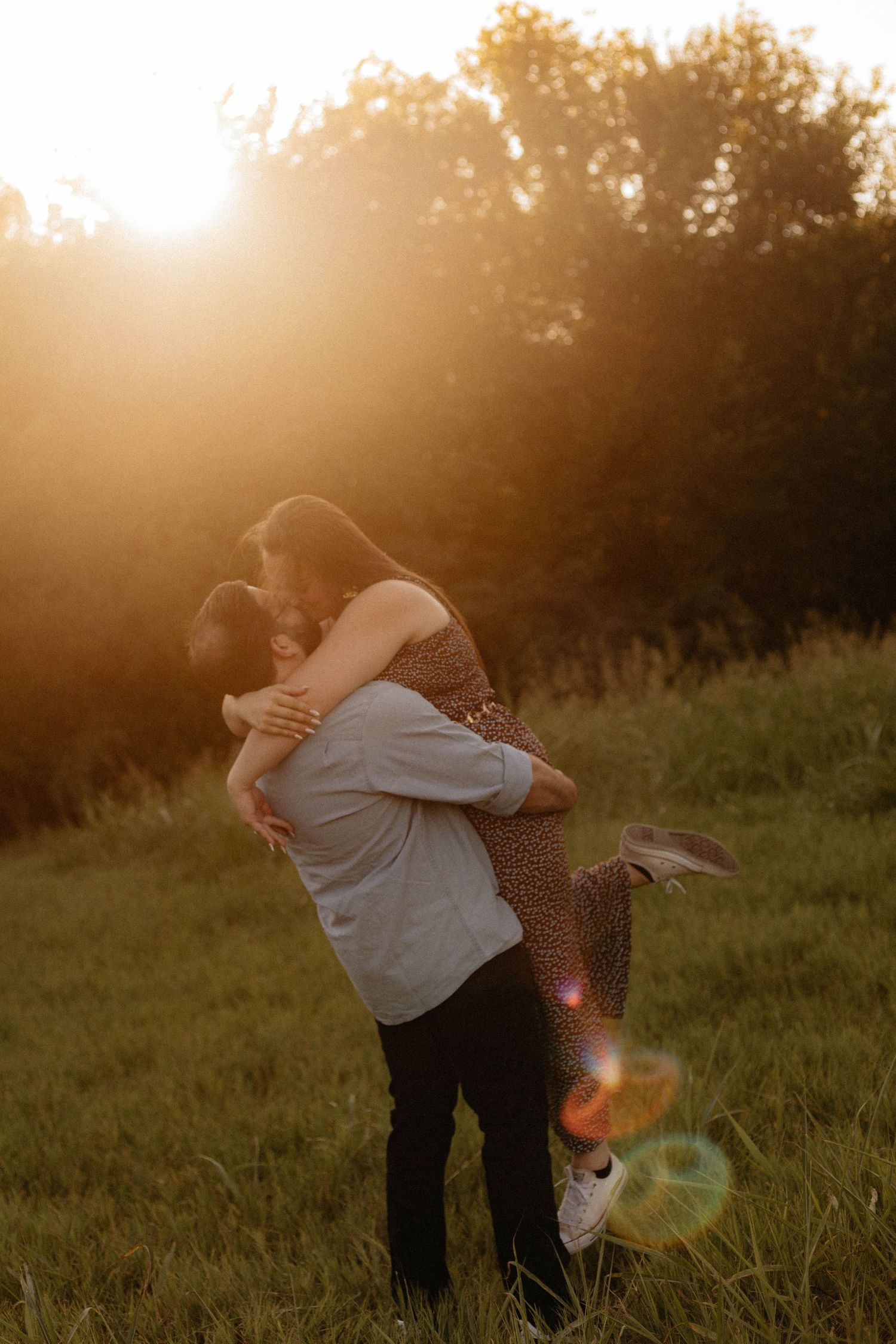 A couple spins and embraces in a sunlit field during golden hour.