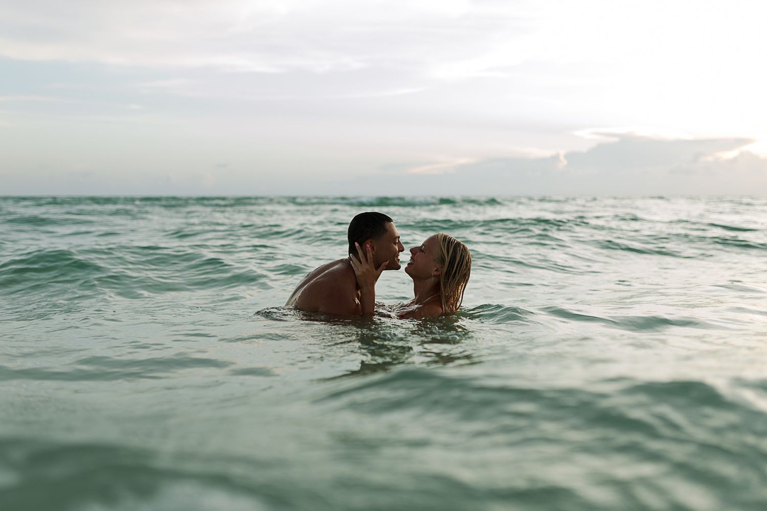 A couple shares an intimate moment while swimming in ocean waters at sunset.