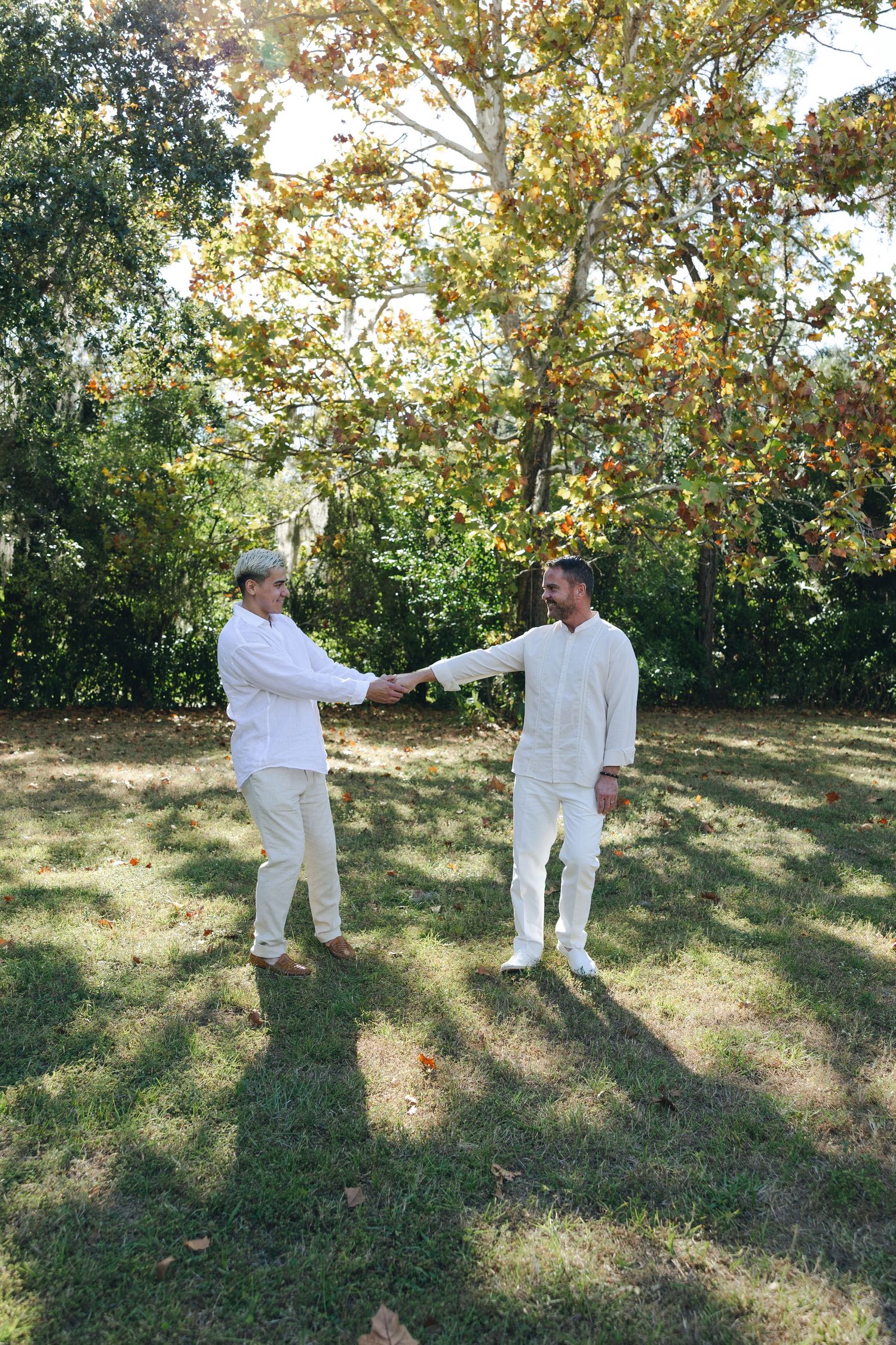 Two people in white outfits practice martial arts moves on a grassy lawn with trees in the background.