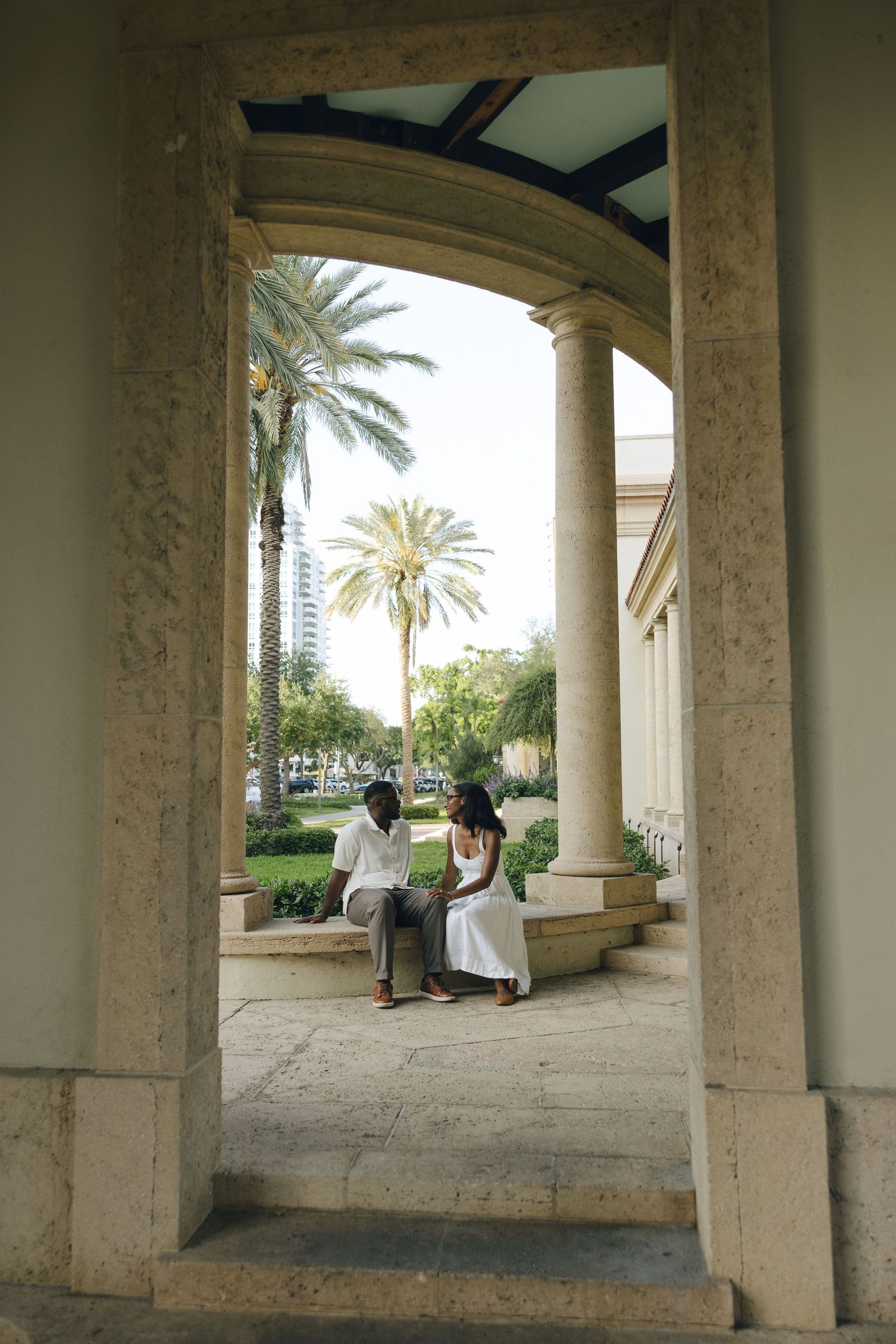 Elegant archway framing two people sitting beneath palm trees in formal attire.