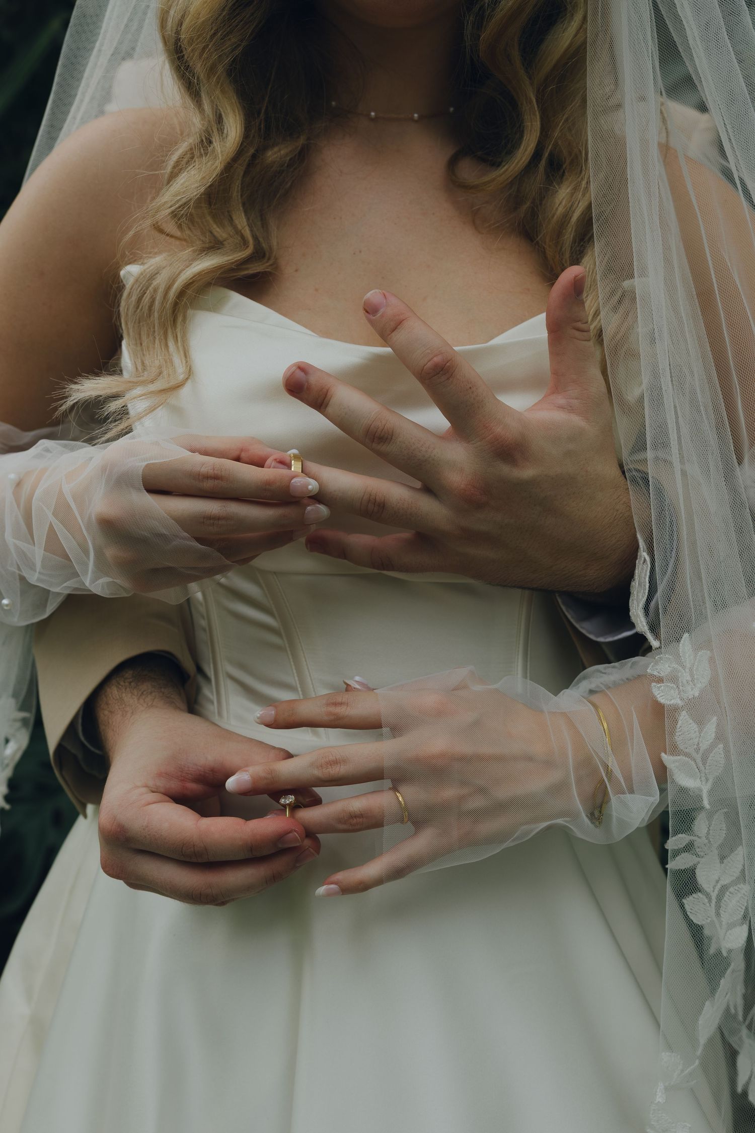 Artistic close-up of bride's hands and wedding dress details showing rings and lace.