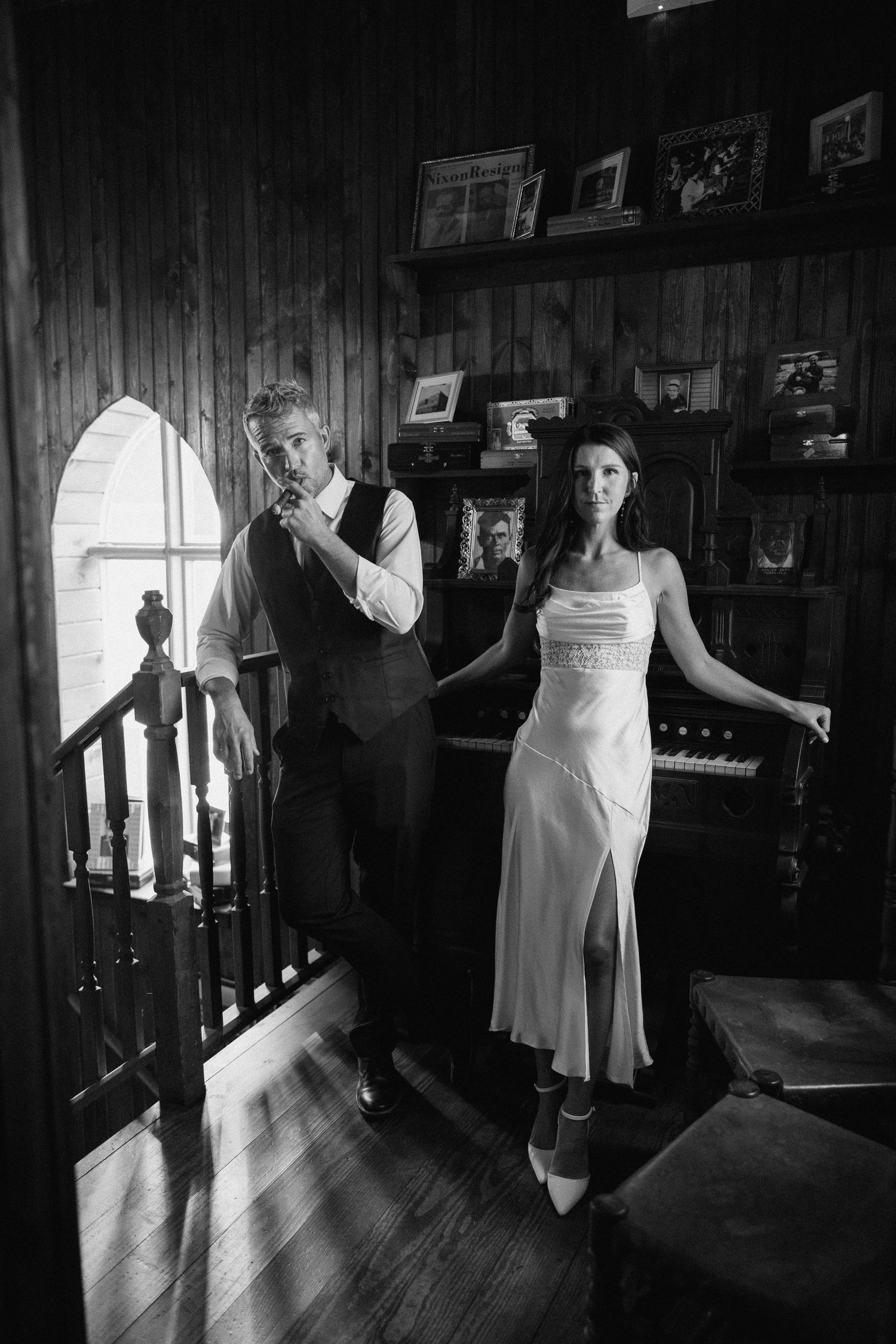 Vintage-style black and white portrait of couple in formal wear inside a rustic wood-paneled room.