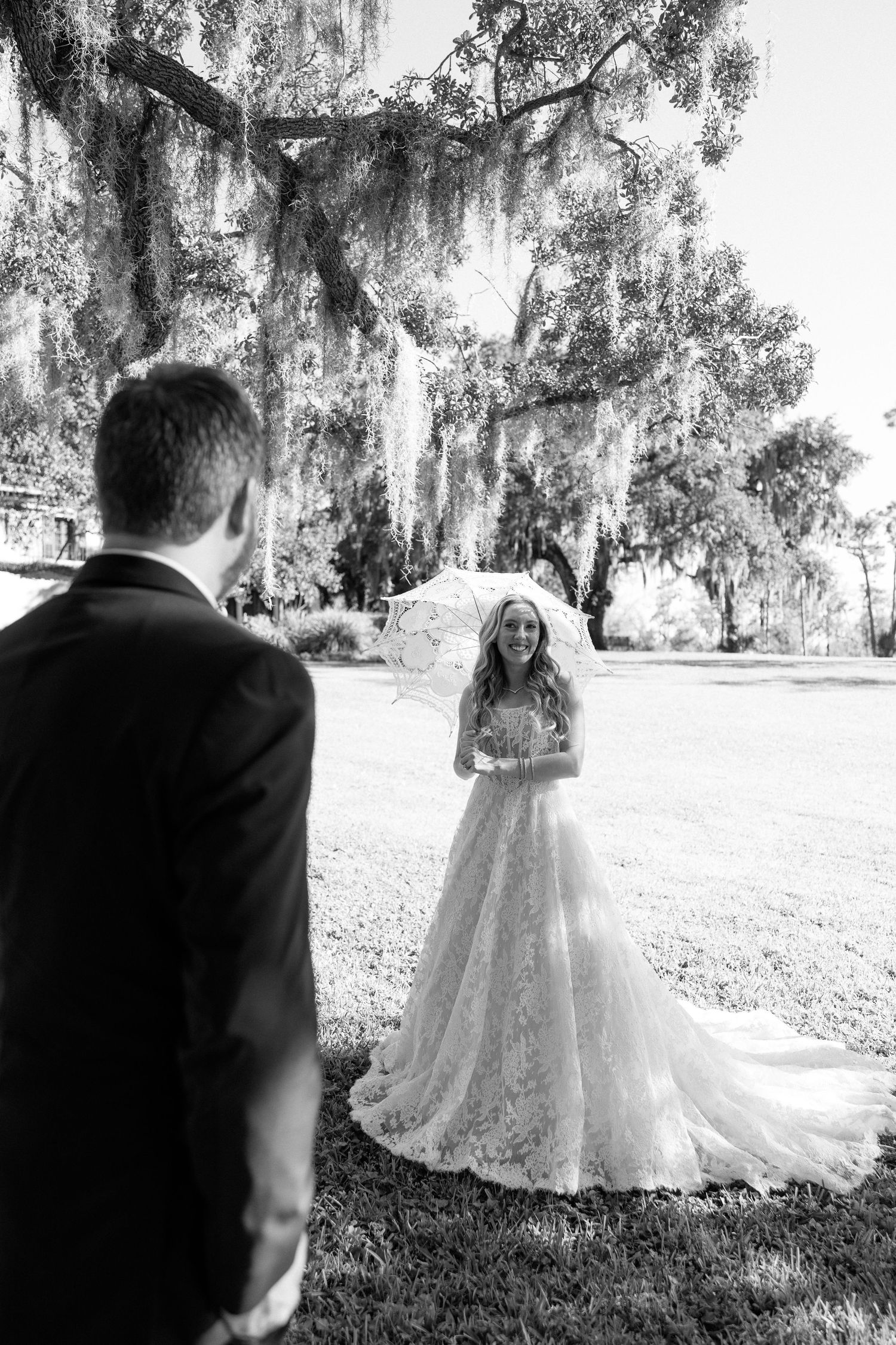 A romantic first look moment between newlyweds under Spanish moss draped trees in a dreamy garden setting.