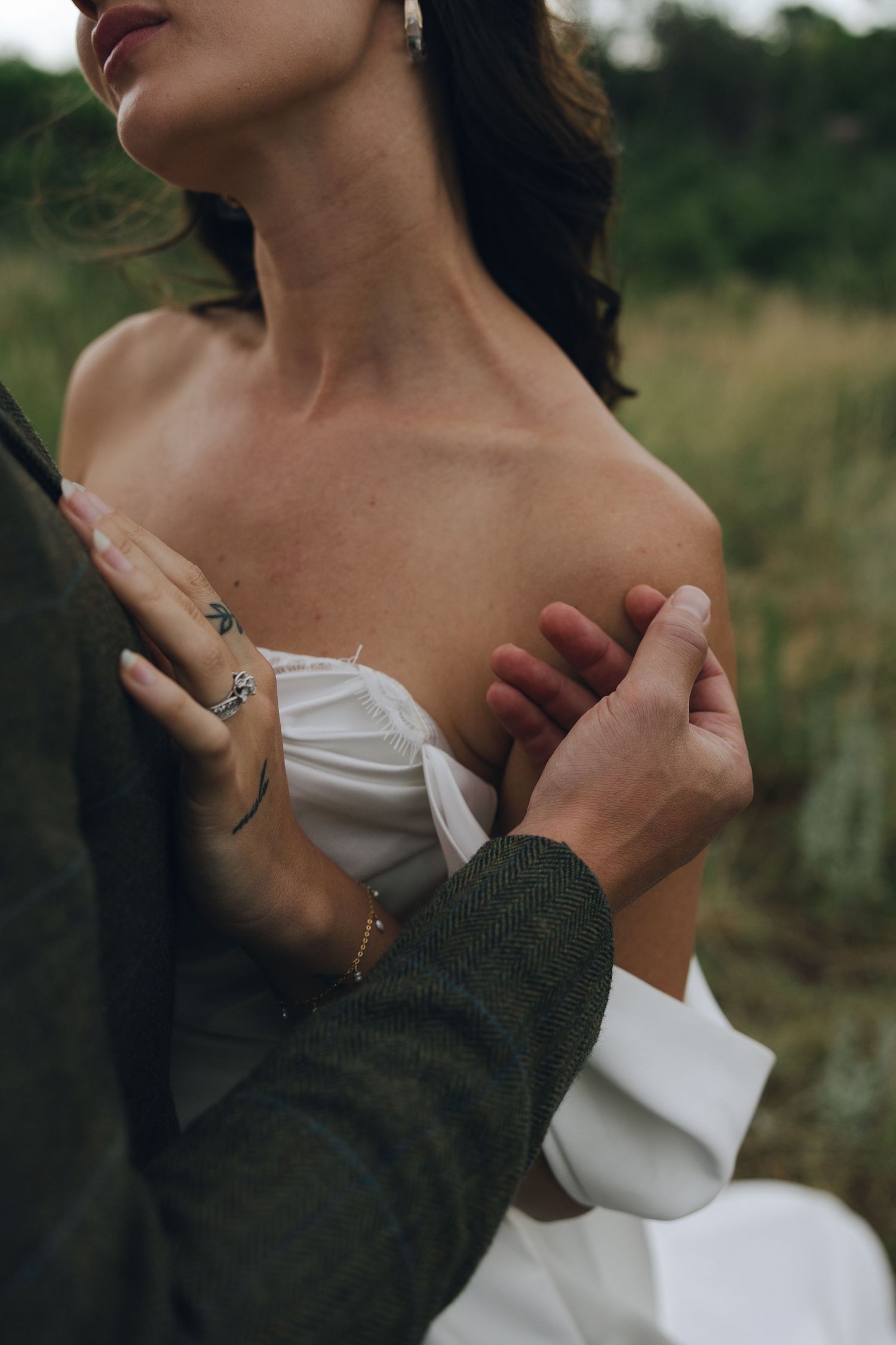 Romantic couple embraces outdoors showing intimate details of white dress and dark sweater in artful portrait series.
