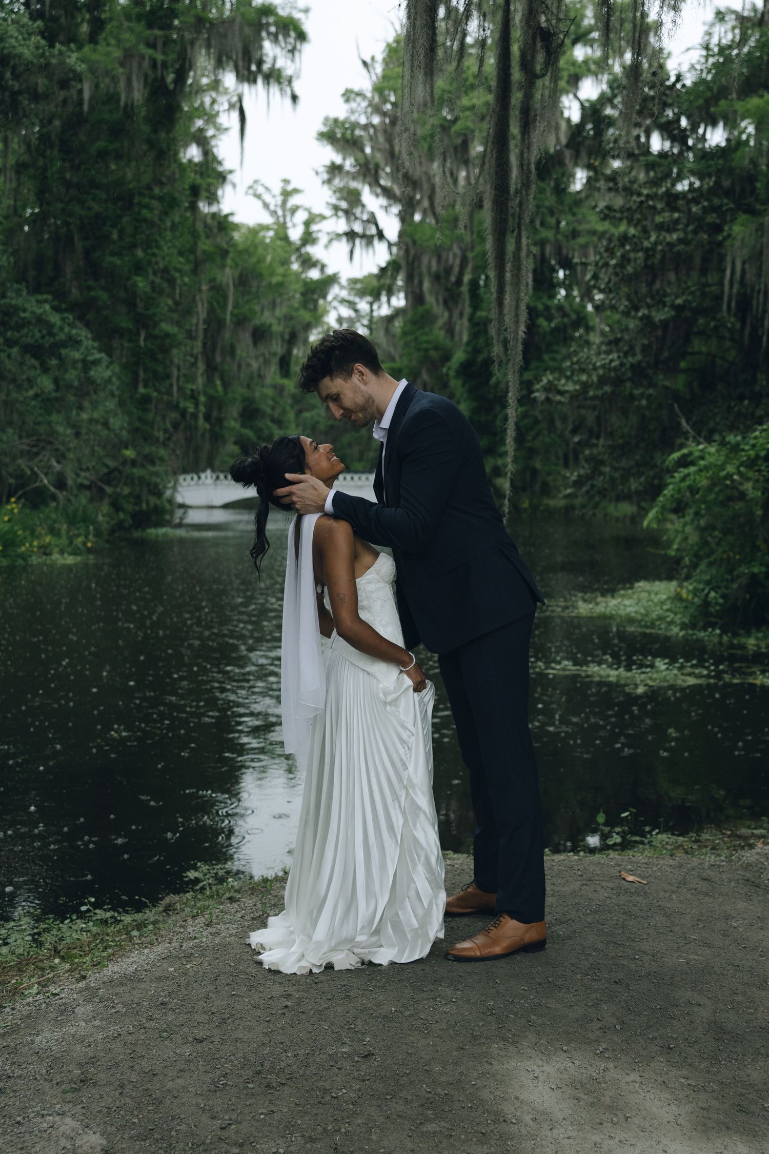 A romantic moment between newlyweds by a serene lake with Spanish moss draped trees.