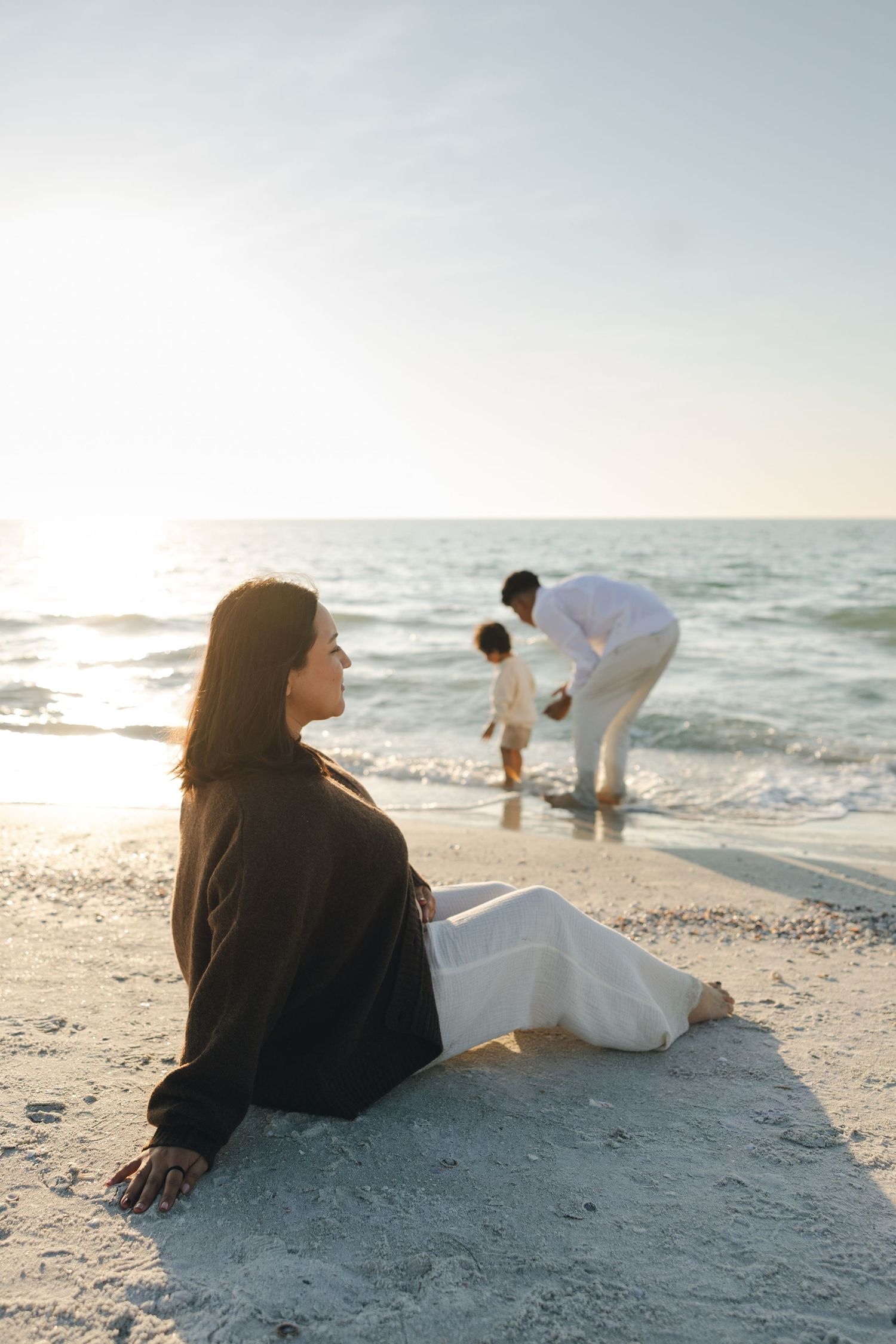 Two people relax on a sandy beach at sunset while gentle waves roll in from the ocean.
