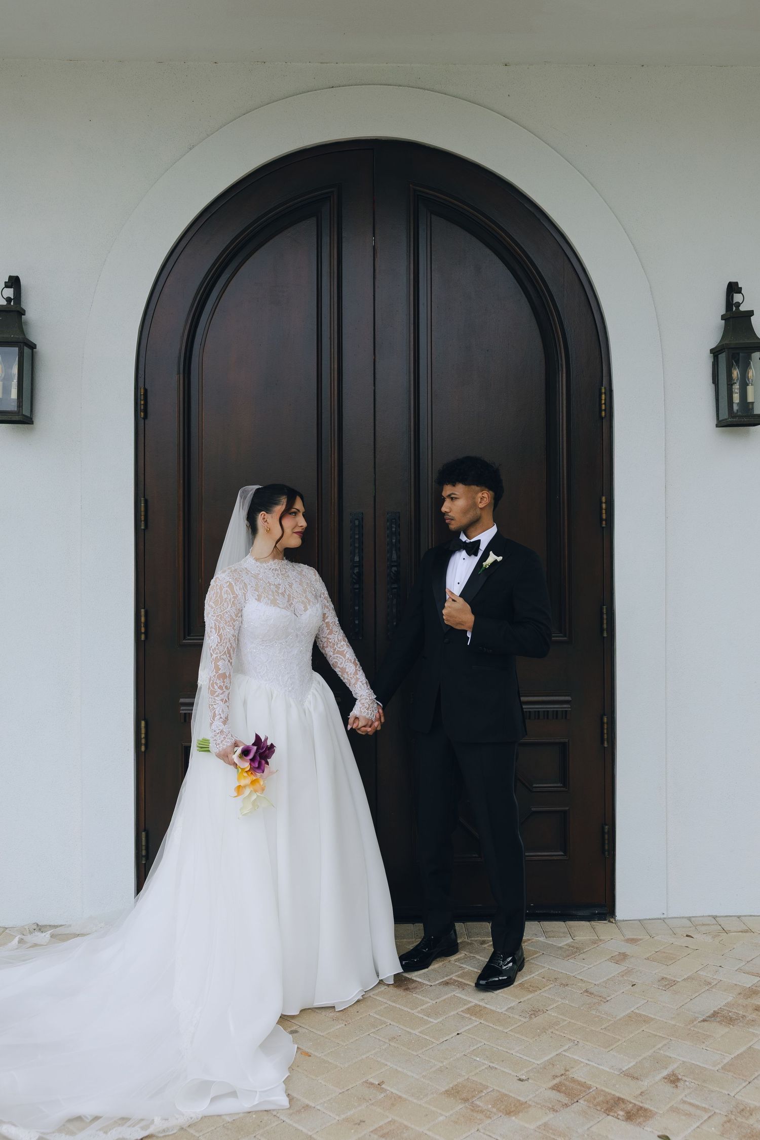 A bride and groom share a tender moment together in front of an arched wooden door at their wedding.