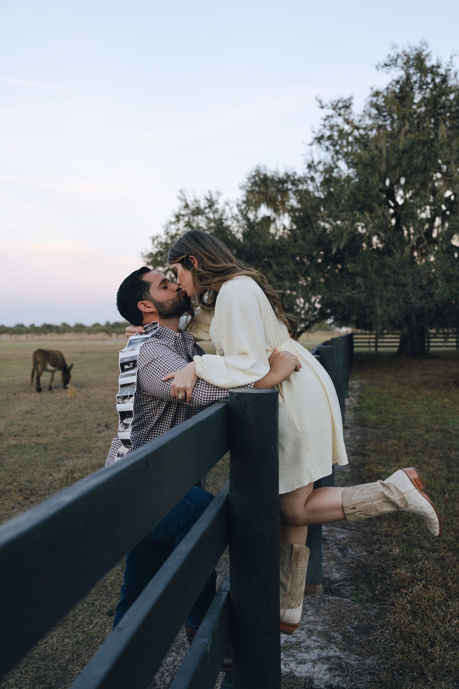 A couple embraces and dances together in a field at sunset with horses grazing in the background.