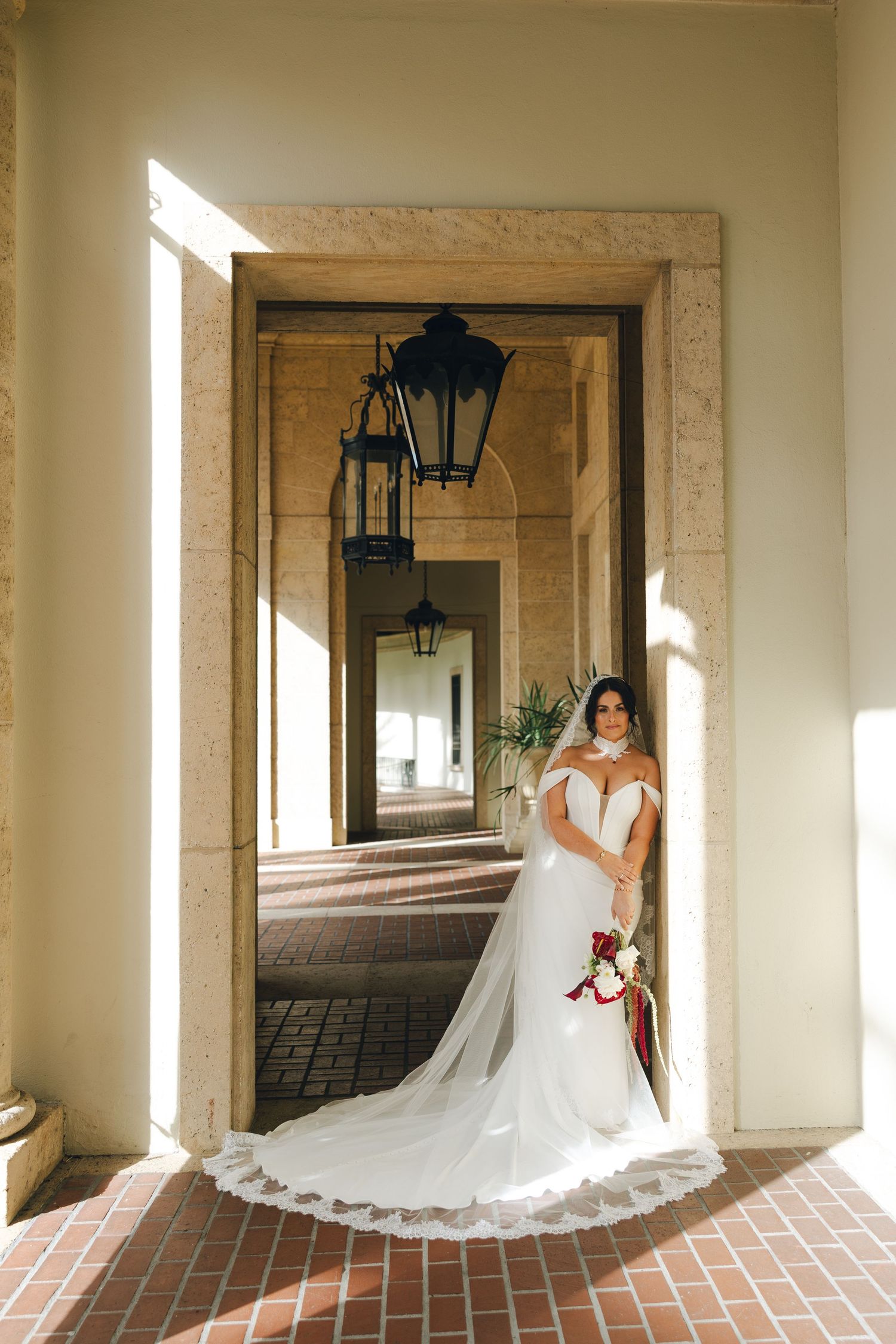 Elegant wedding dress with long lace train displayed in a columned archway with hanging lanterns.