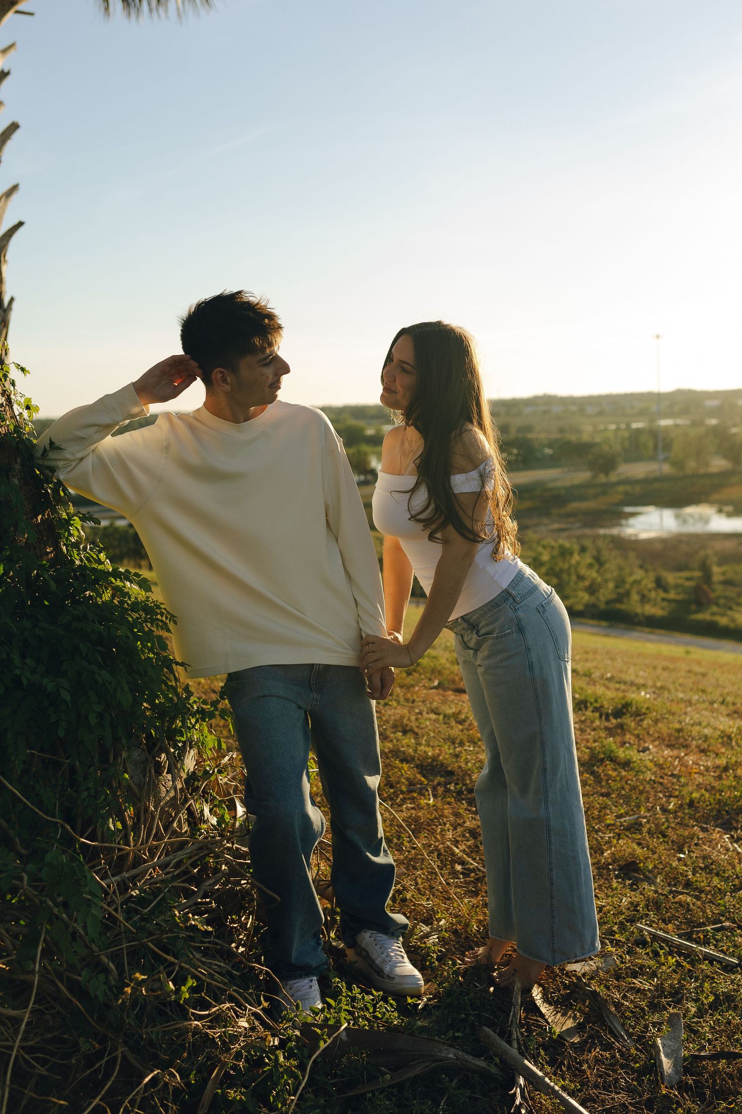 A couple holds hands while standing on a scenic hillside during sunset.