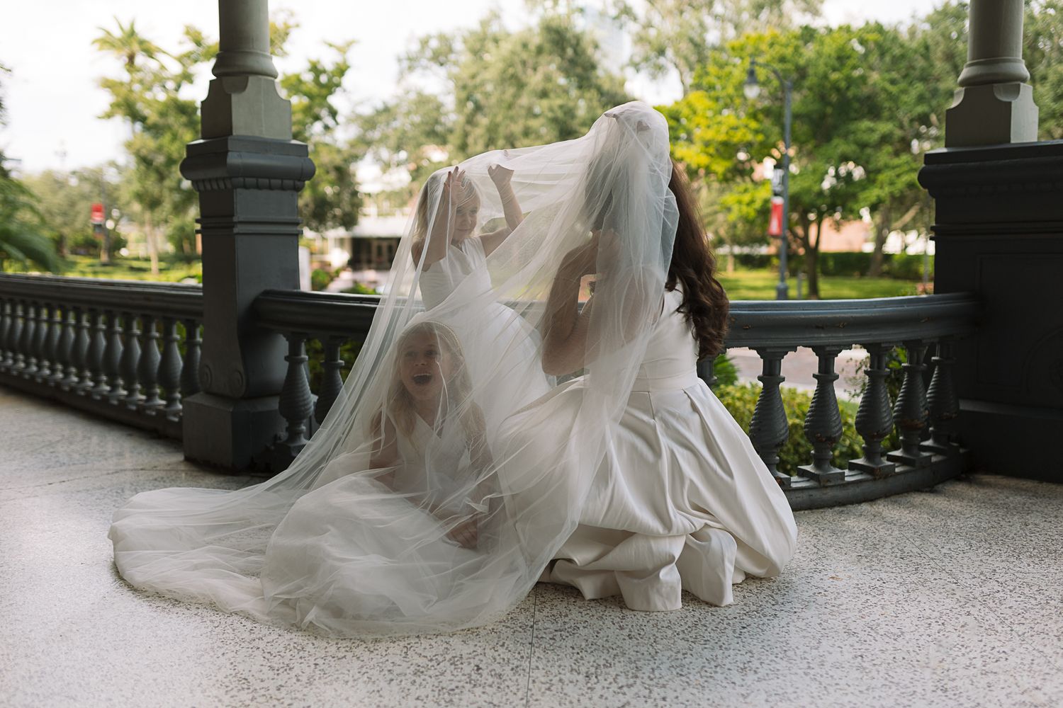 Long flowing white wedding dress and veil spread across stone terrace in elegant outdoor setting.
