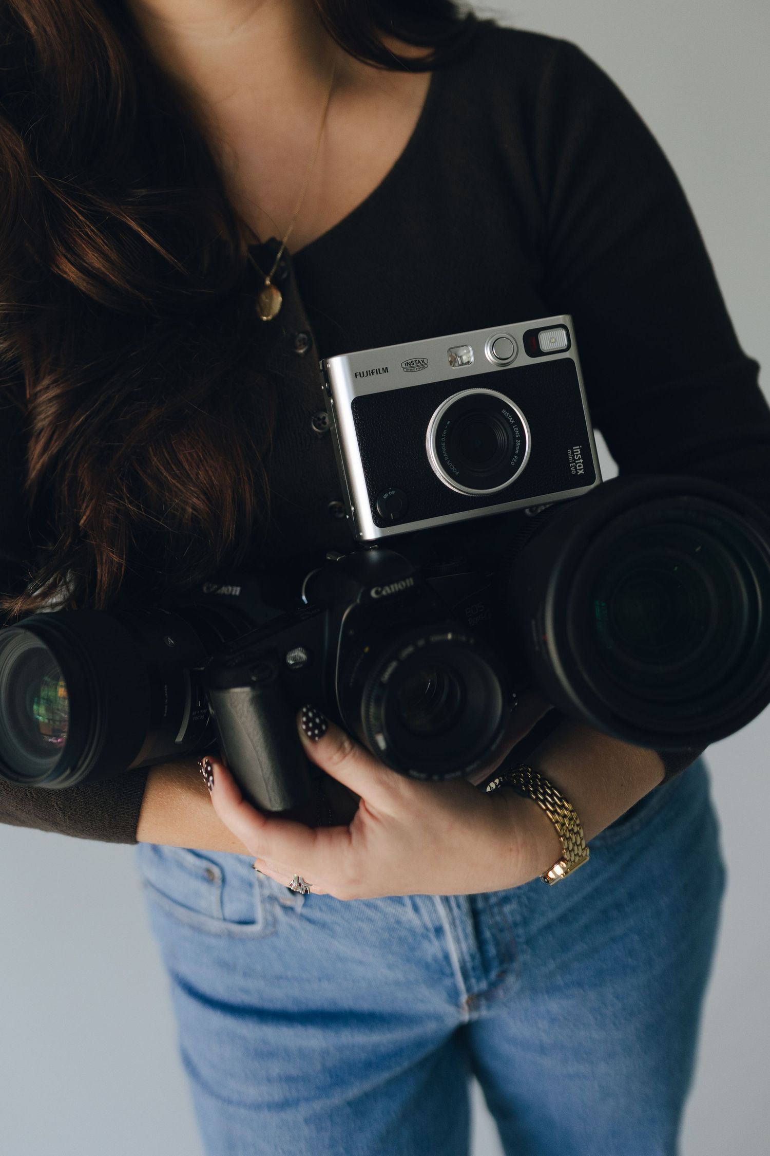 Person in black sweater and jeans holding a vintage film camera against a light gray background.