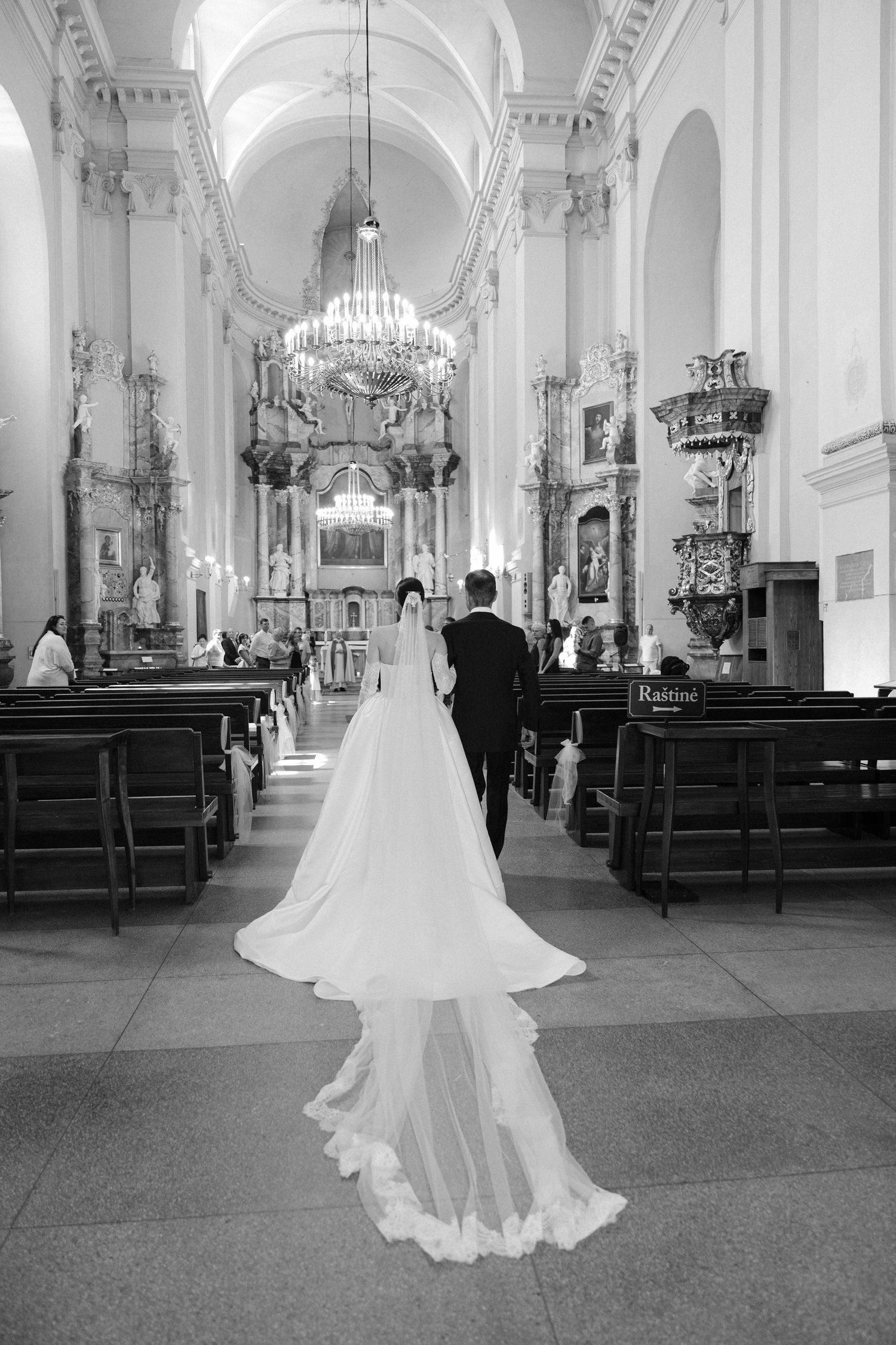 Bride and groom walk down the aisle of an ornate baroque church in a stunning black and white wedding photo.