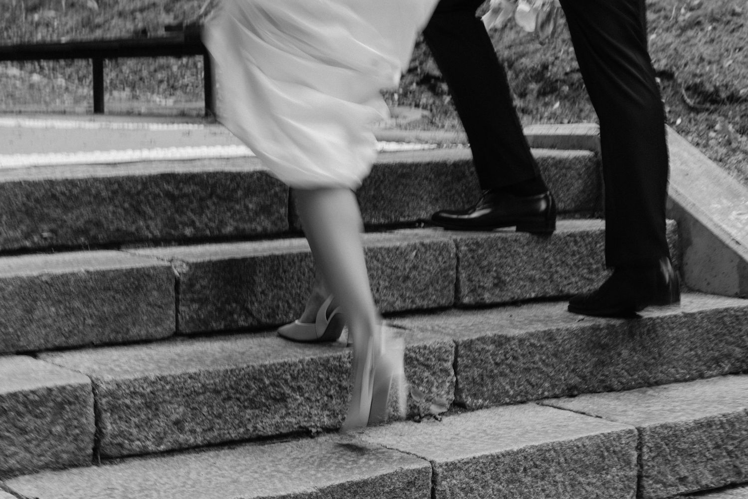 Black and white photo of a bride and groom walking up stone steps after their wedding ceremony.
