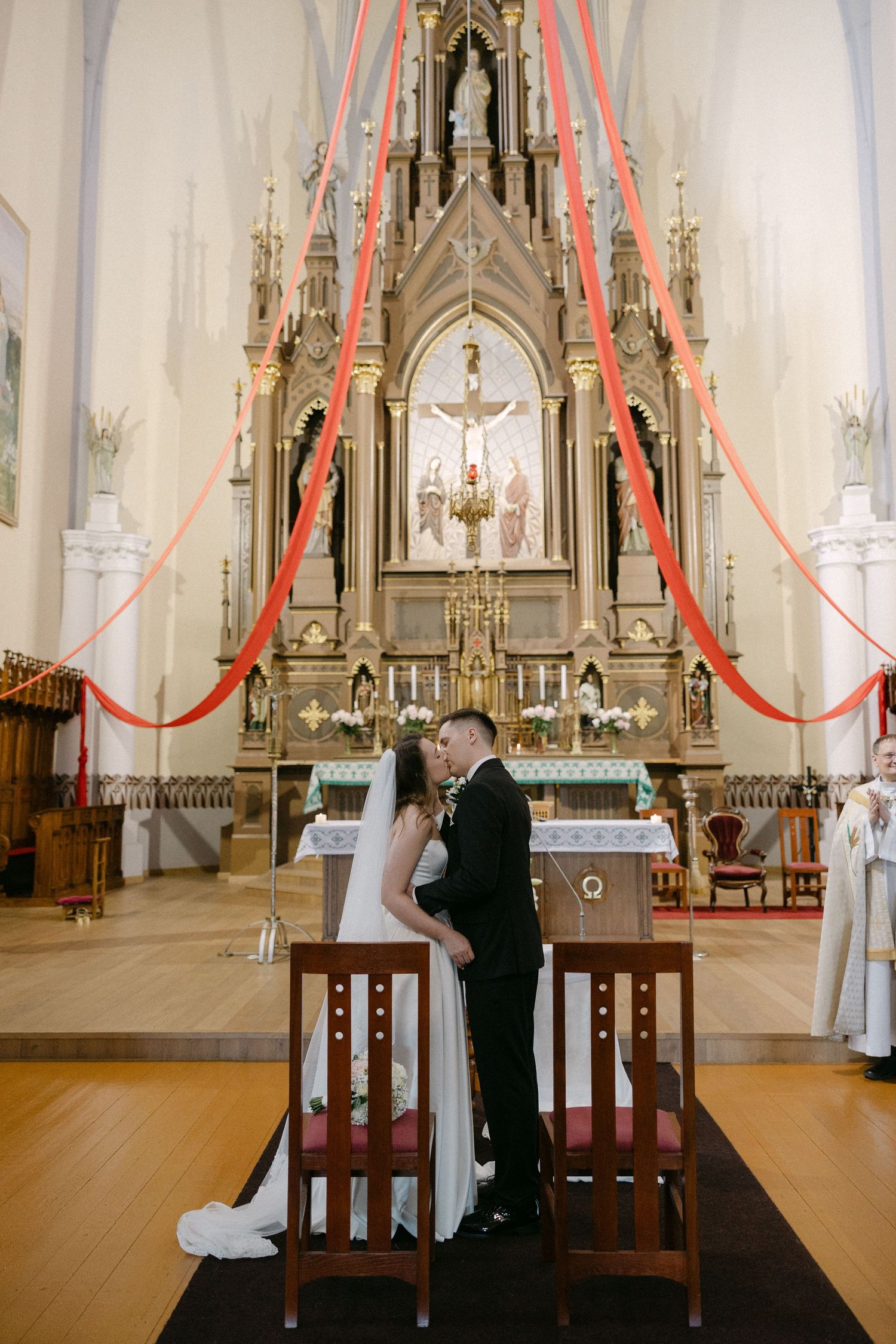 Bride and groom share a kiss at the altar during their wedding ceremony in an ornate Catholic church.