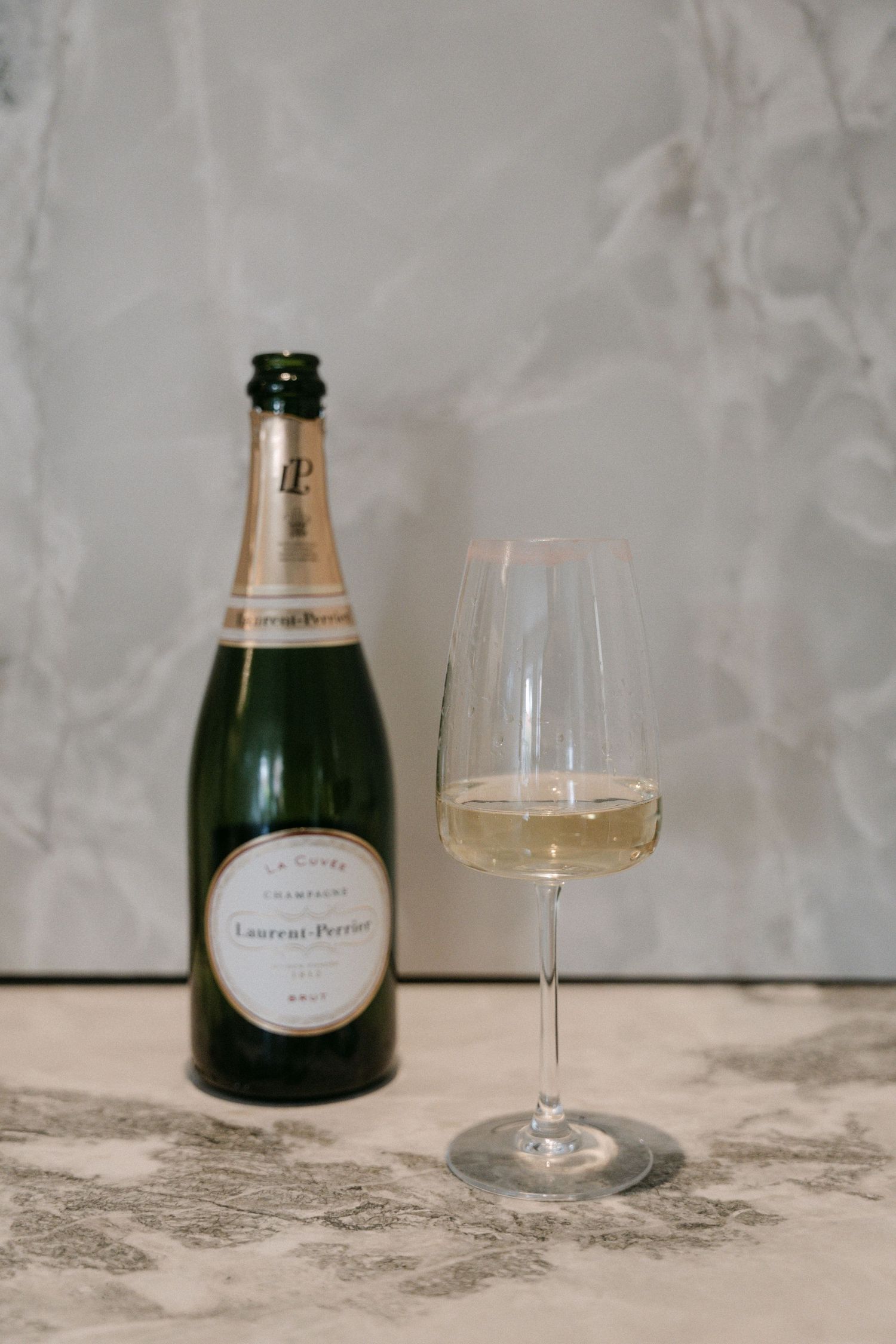 Laurent-Perrier La Cuvee Brut Champagne bottle beside a filled crystal flute glass on marble surface.