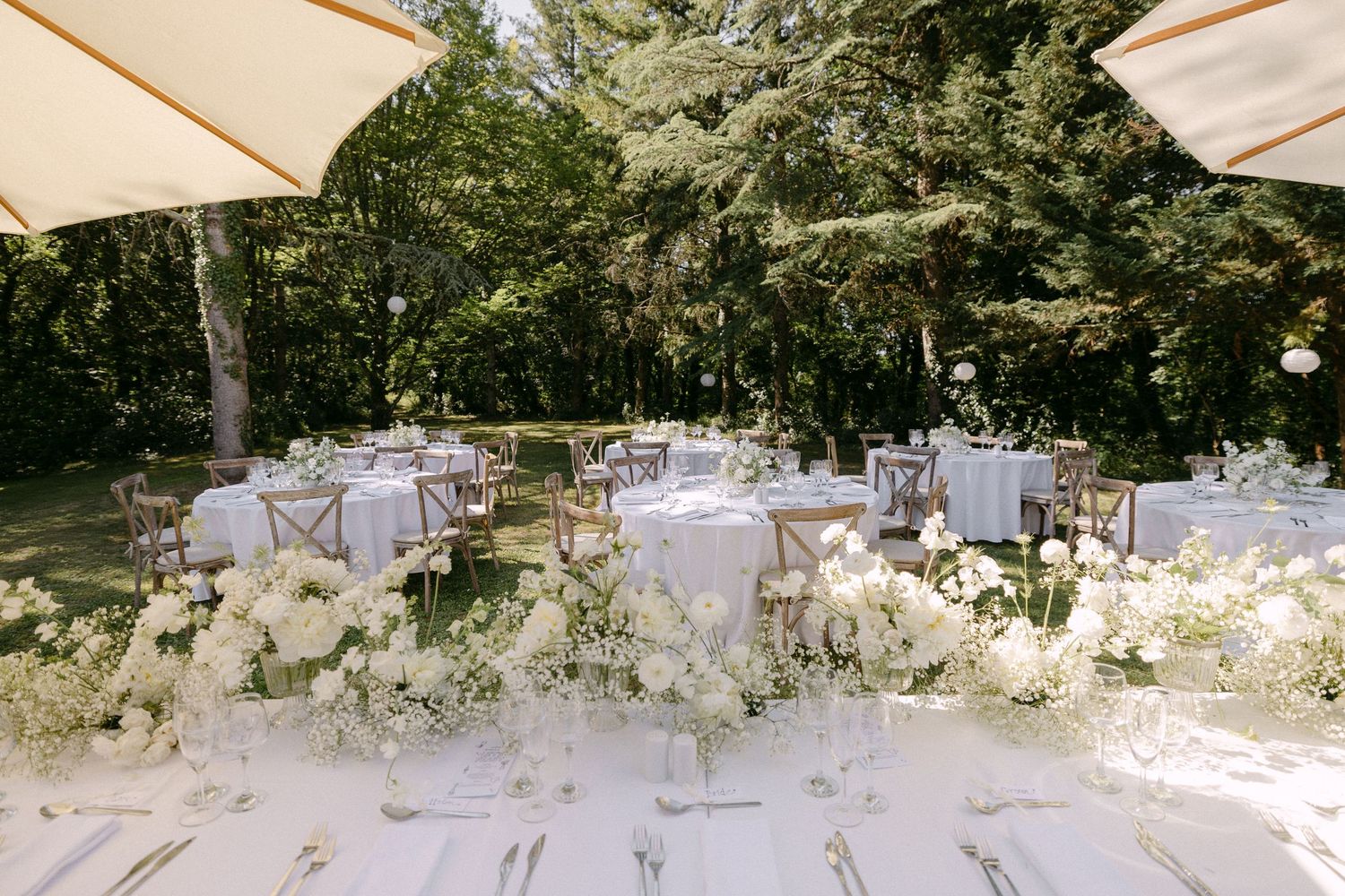 Elegant outdoor wedding reception with white floral centerpieces, round tables, and garden surroundings.