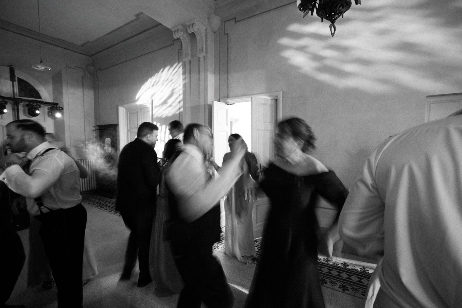 Black and white photo of wedding guests dancing energetically in elegant ballroom reception venue.