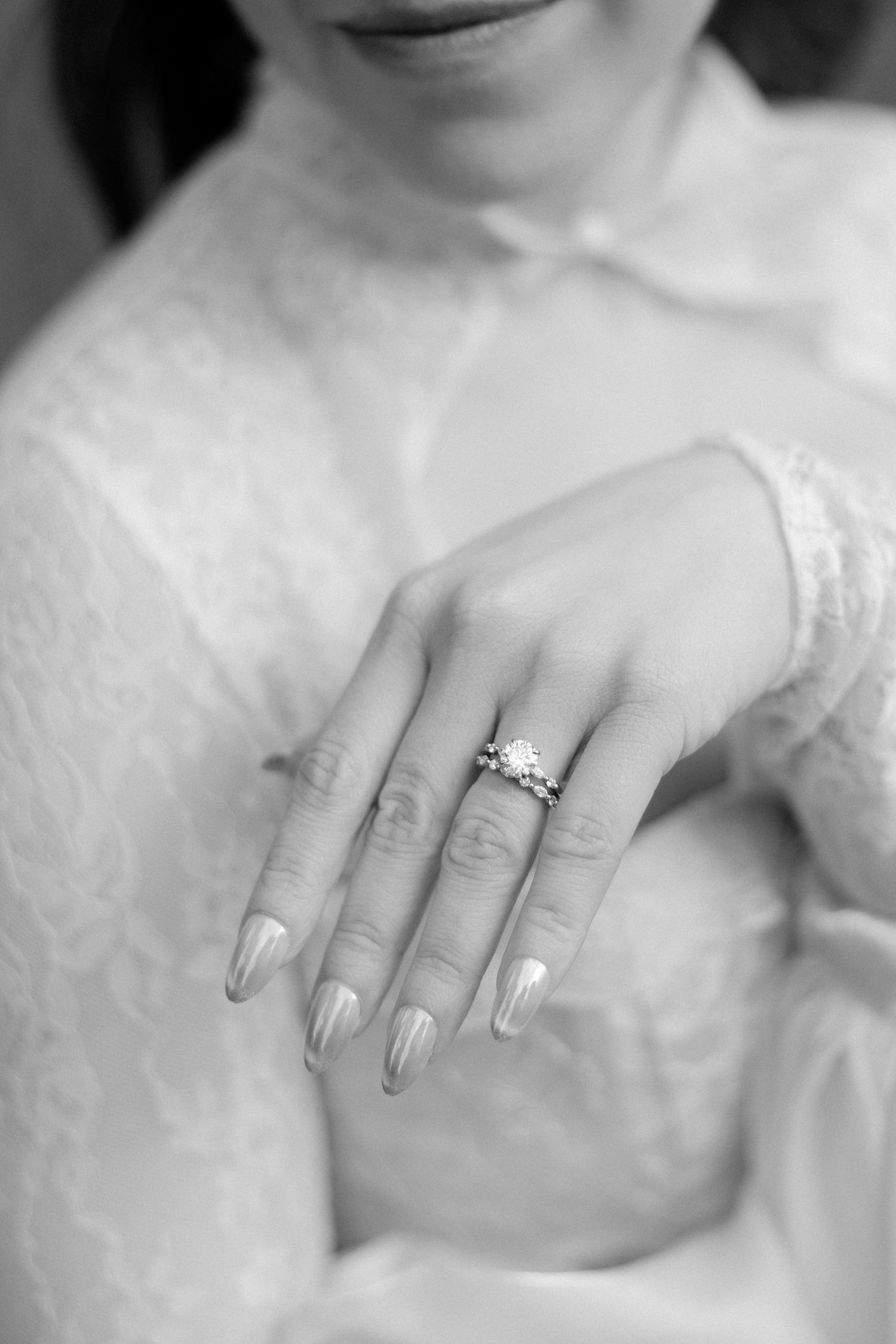 Black and white close-up of bride in lace dress showcasing elegant diamond engagement ring.