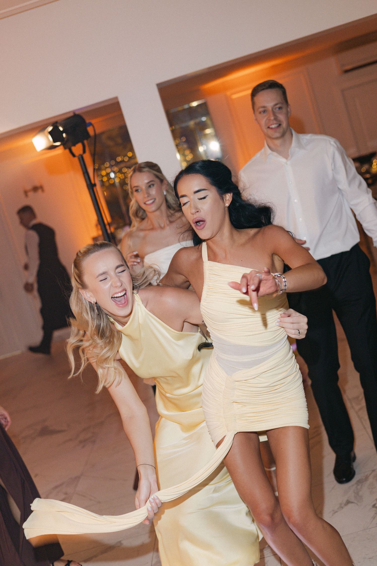 Energetic wedding guests in yellow and black dresses dancing and celebrating at a lively reception.