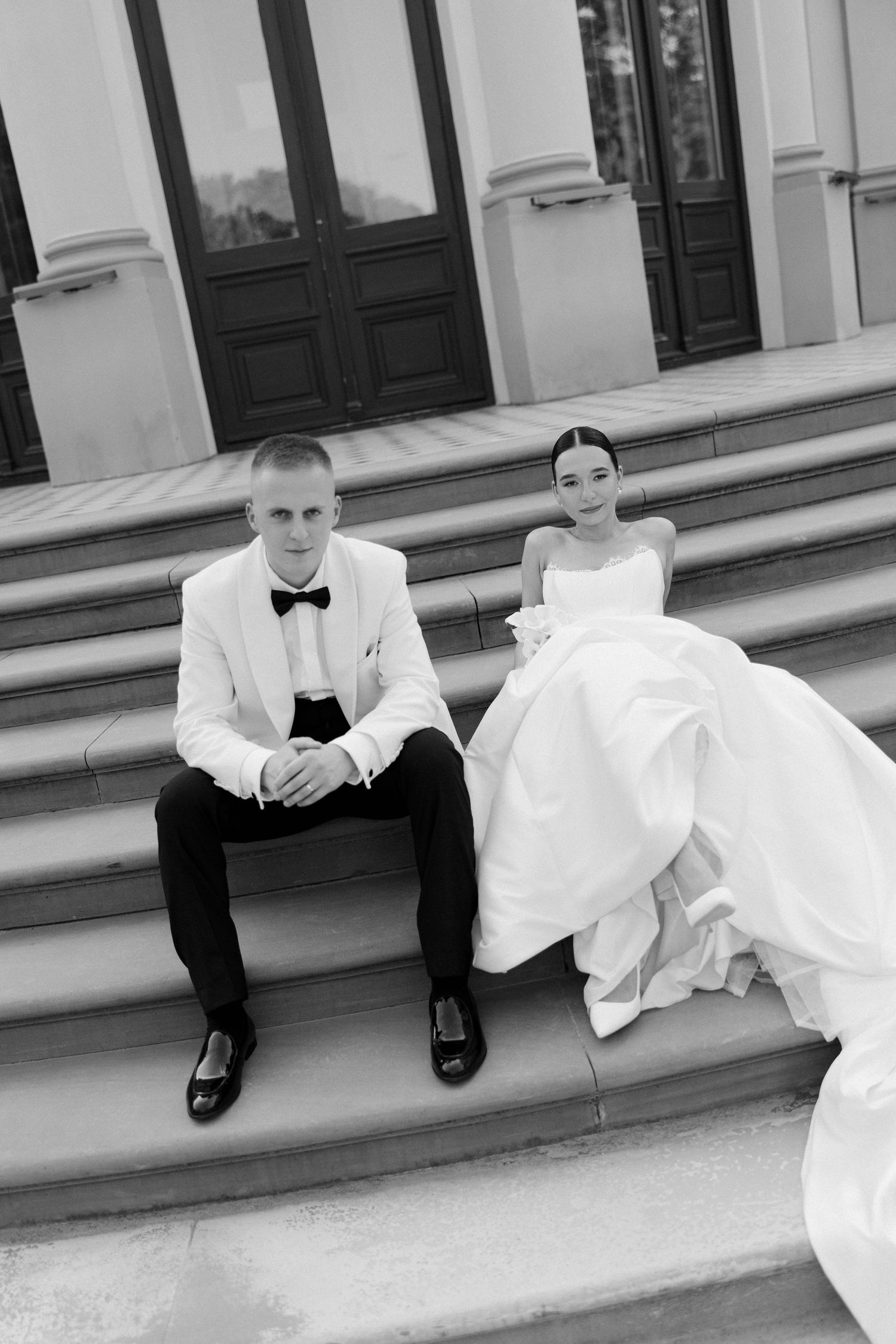 Black and white portrait of bride and groom sitting on steps of neoclassical building.