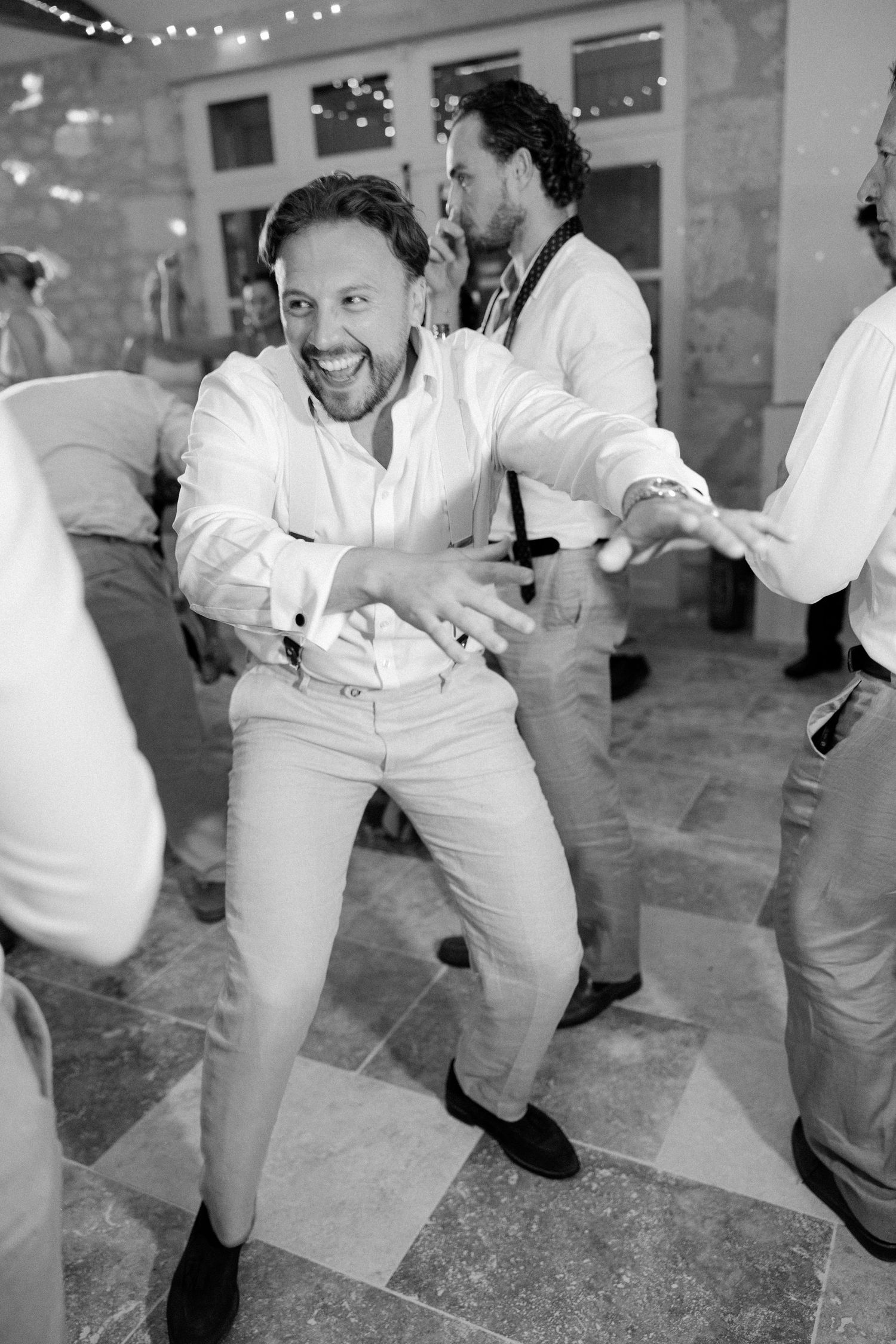 Man dancing energetically at a wedding reception in black and white photo with guests celebrating in background.