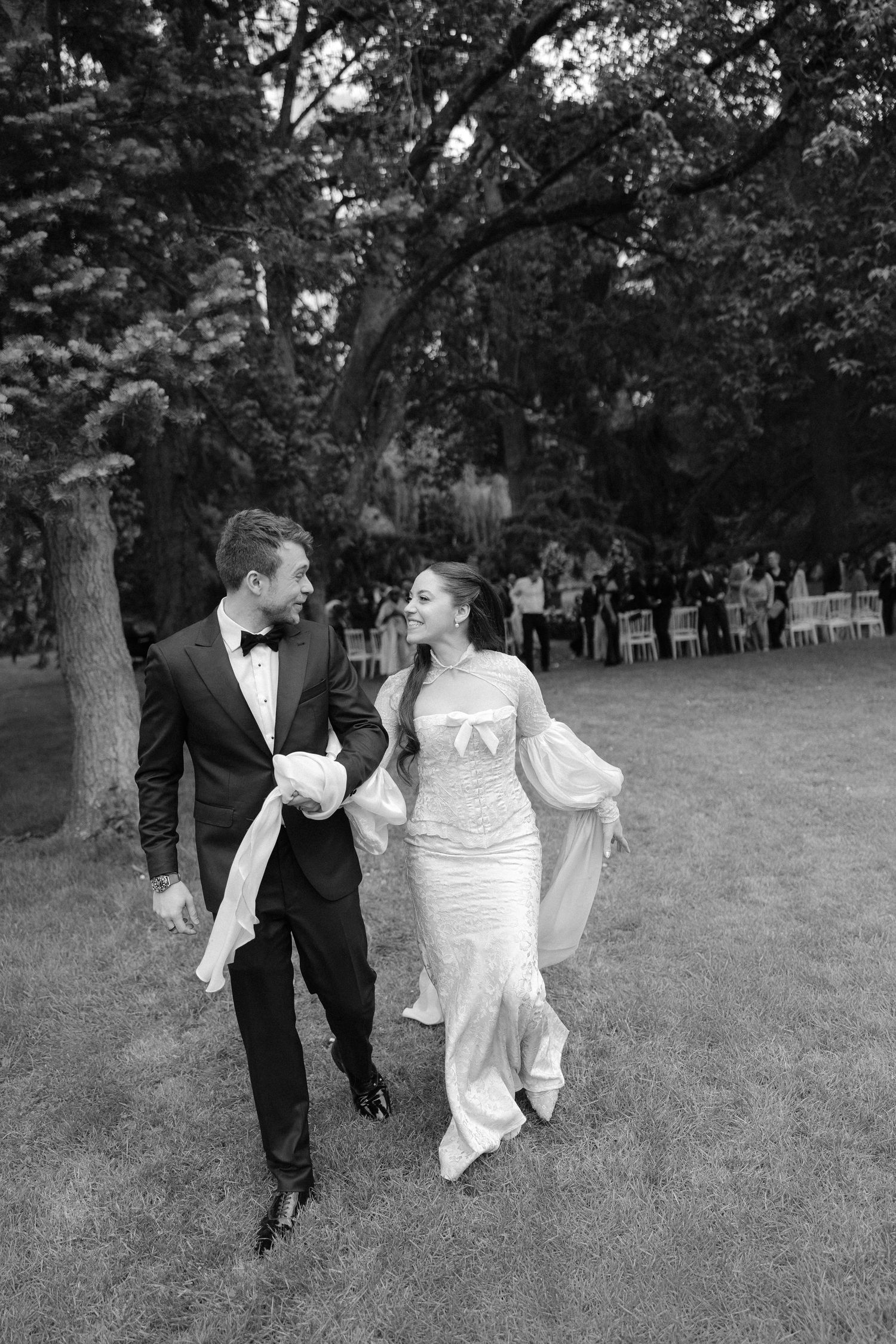 Bride and groom walking hand in hand through garden in black and white wedding photo.