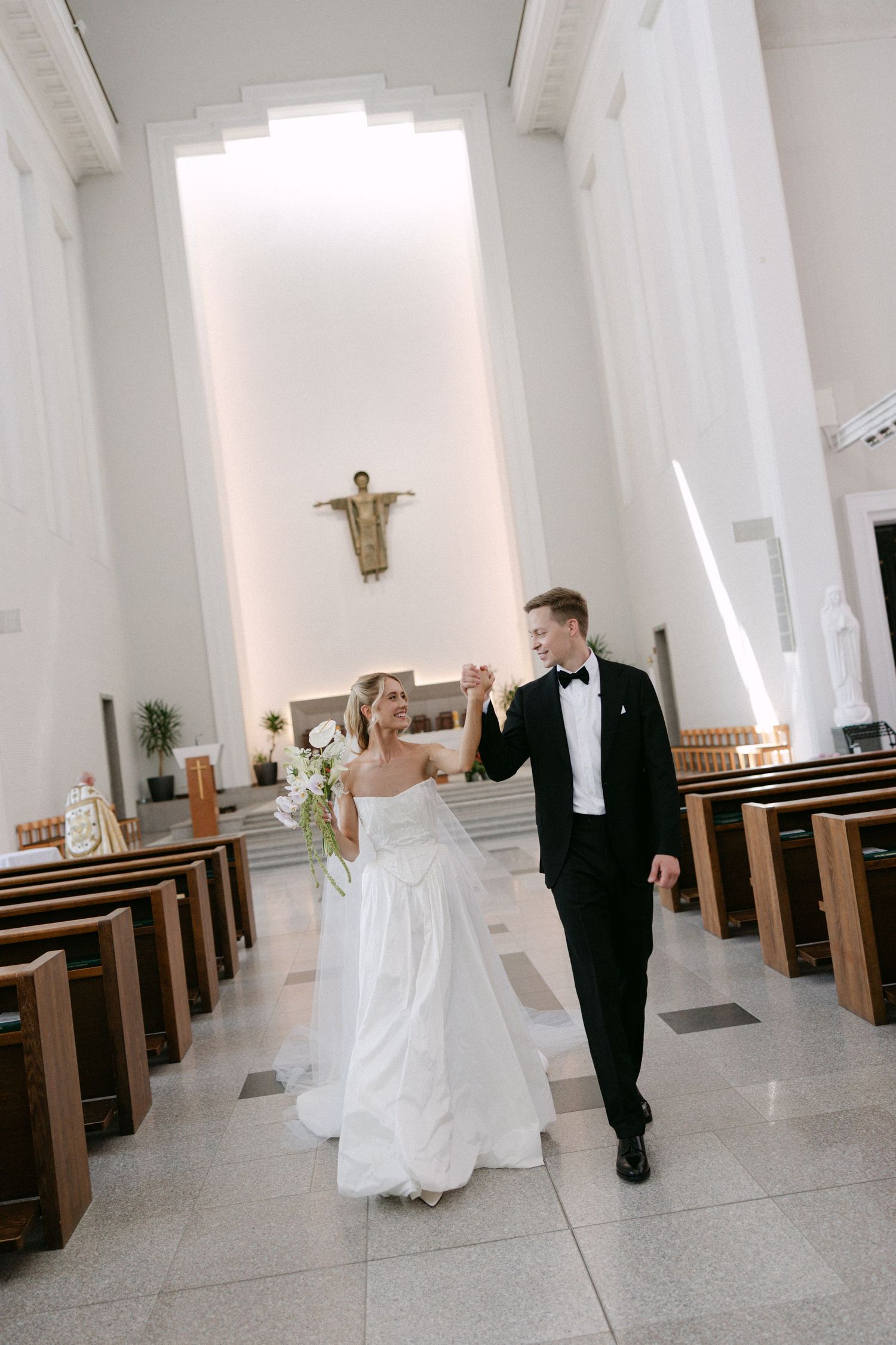 Bride and groom walk hand-in-hand down the aisle of a modern church after their wedding ceremony.