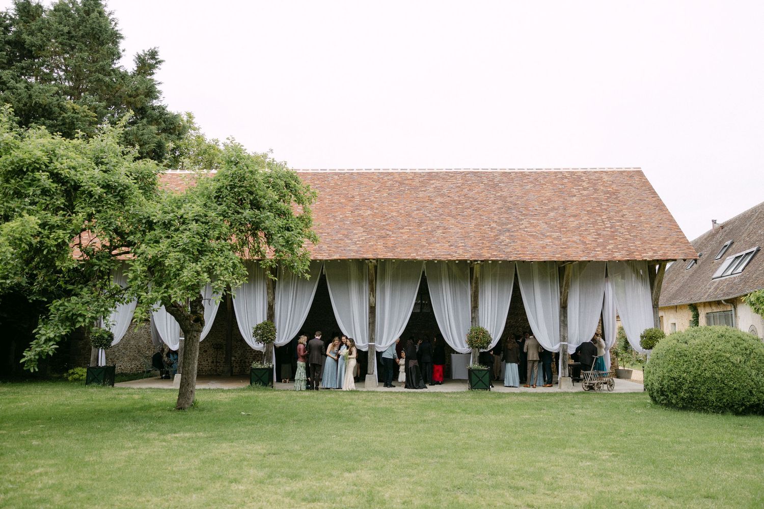 Rustic barn wedding venue with elegant white draping and guests gathering on manicured lawn.