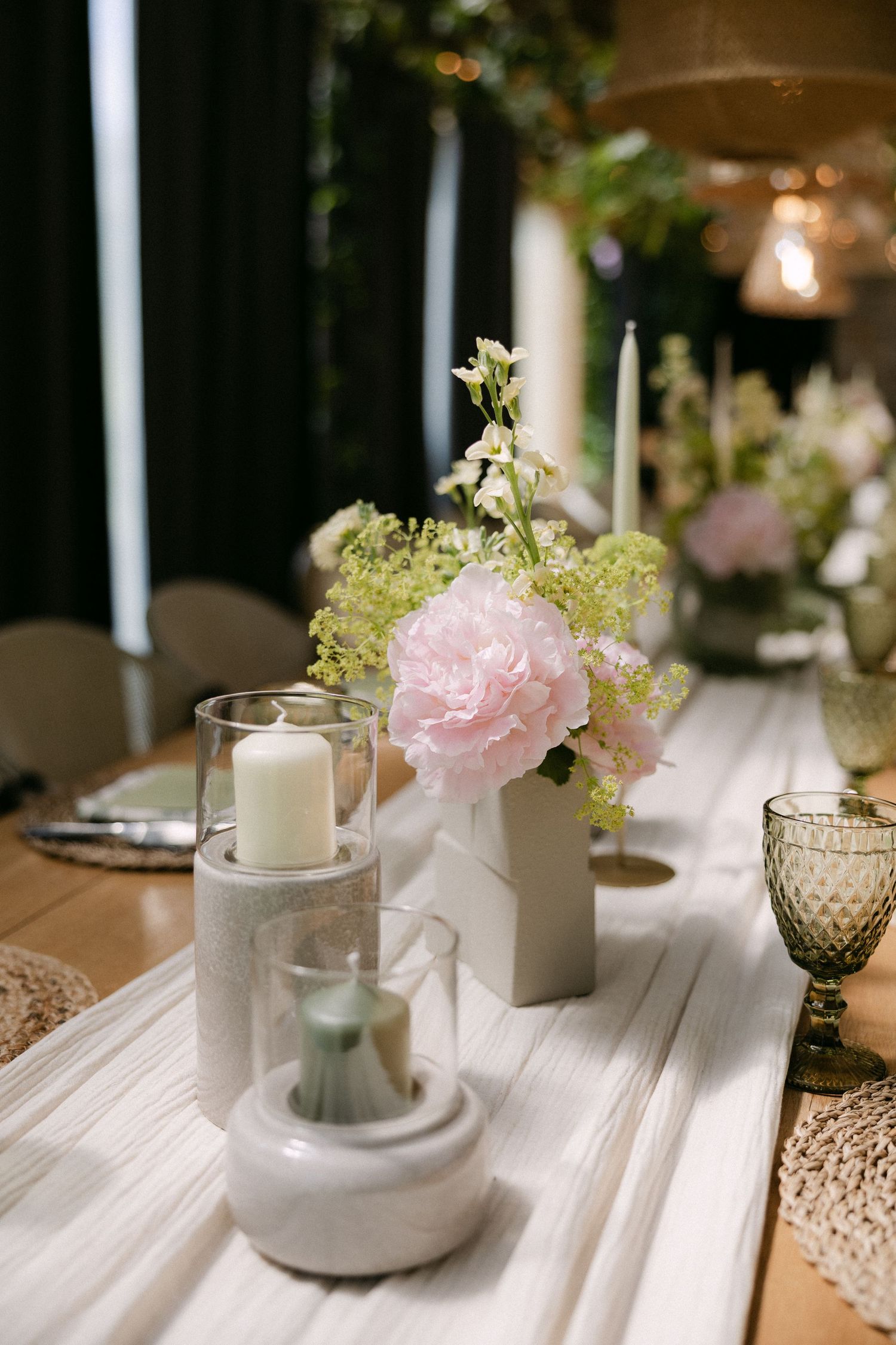 Elegant wedding reception table with pink peonies, white candles, and green florals on a rustic wooden table.