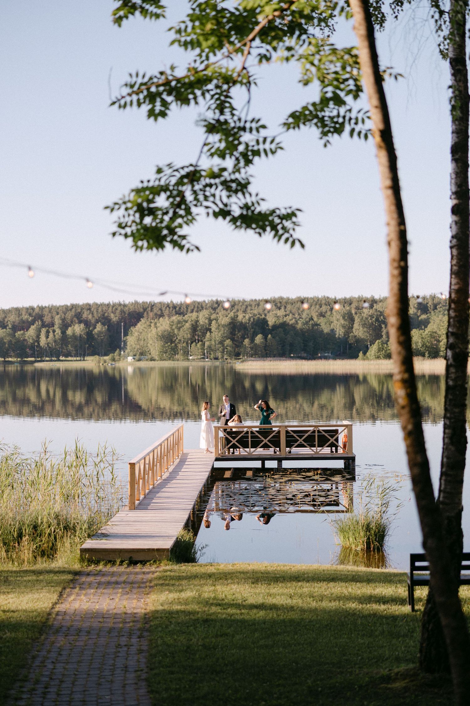 Bride and groom standing on a wooden dock over a calm reflective lake at golden hour.