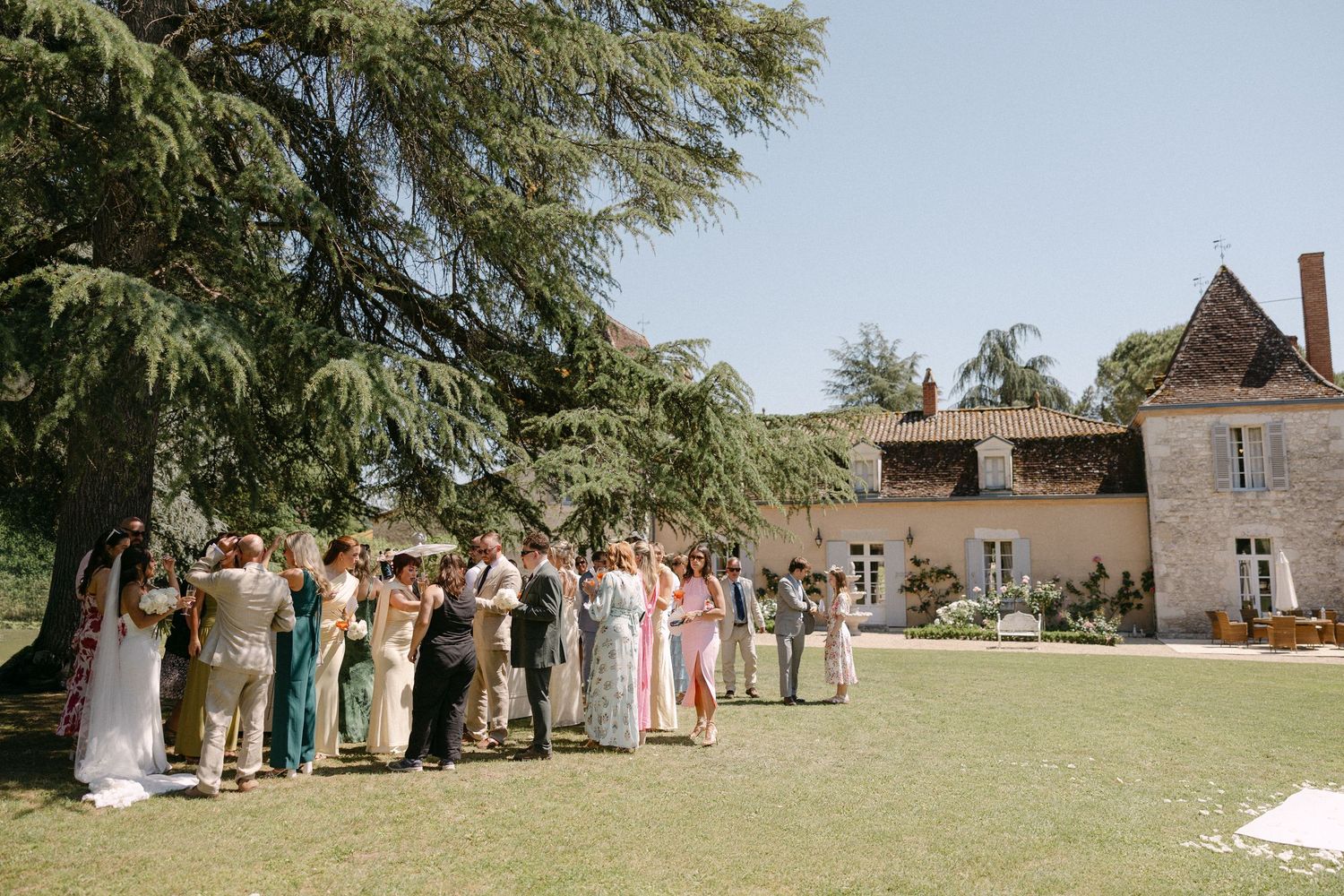 Wedding guests gathered on green lawn outside a charming French countryside chateau.