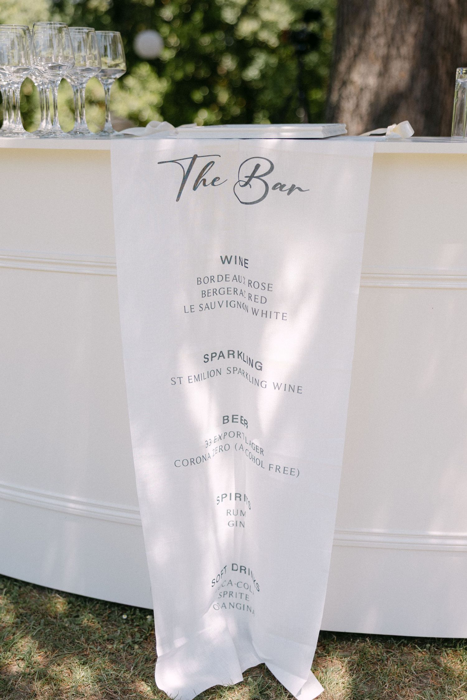 Elegant white bar menu sign listing wines, sparkling, beer, and spirits at outdoor wedding.