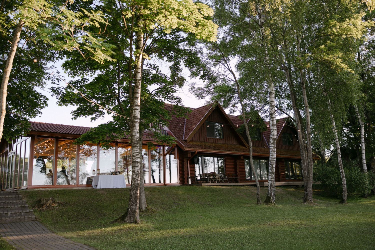 Rustic wooden wedding venue lodge surrounded by birch trees and green lawn in forest setting.
