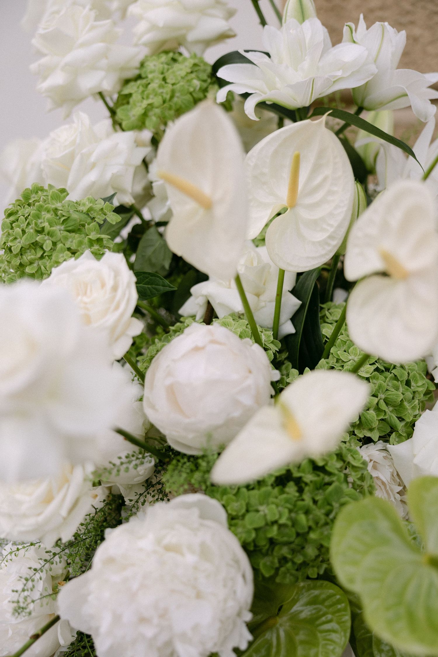 Elegant wedding floral arrangement featuring white anthuriums, peonies, roses, and green hydrangeas in a lush bouquet.