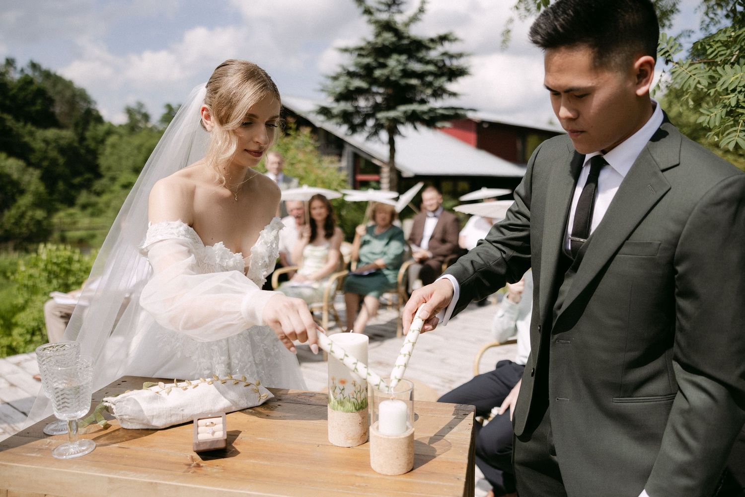 Bride and groom performing sand unity ceremony outdoors with wedding guests seated in background.
