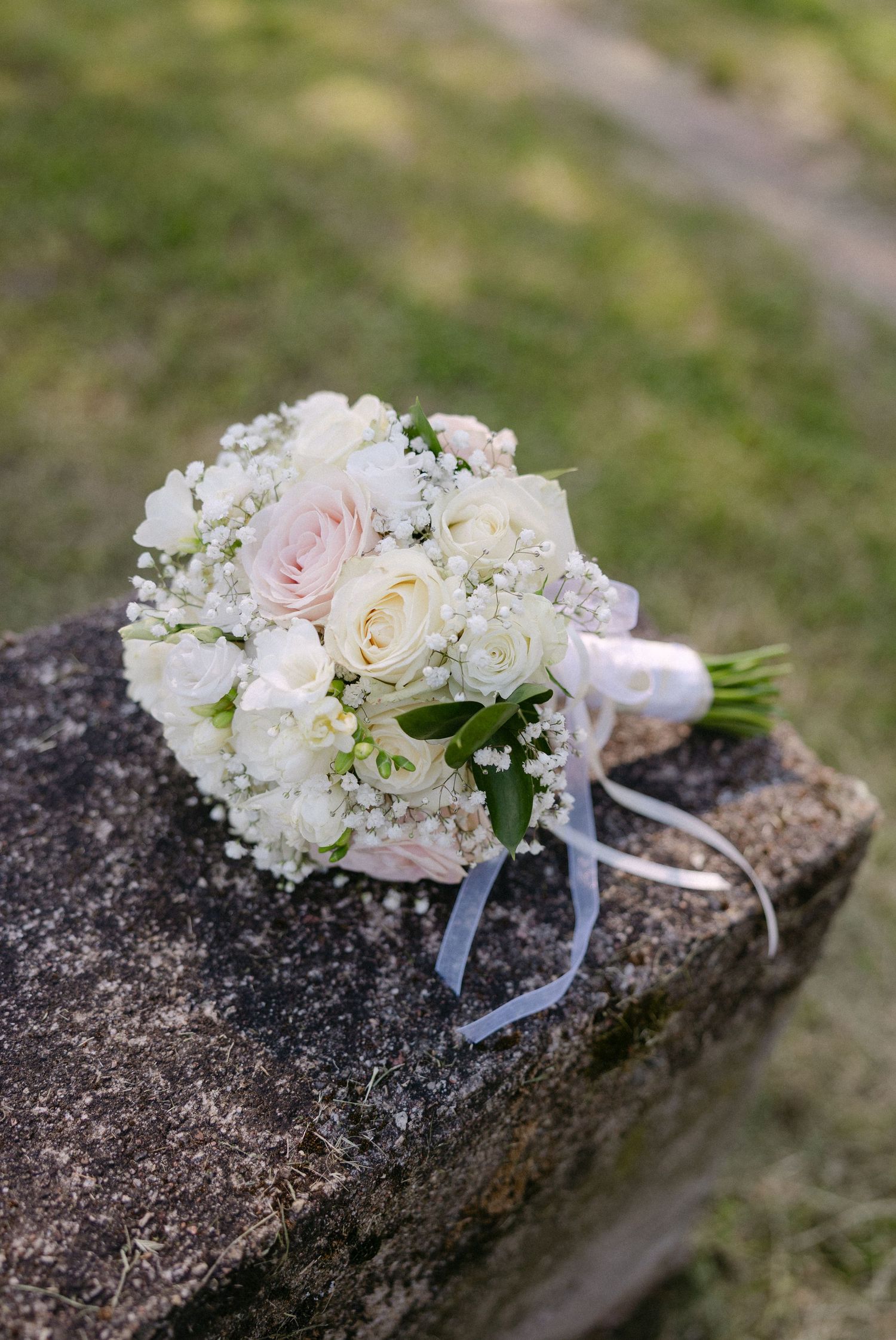 Elegant bridal bouquet of white and blush roses with baby's breath resting on a stone surface.