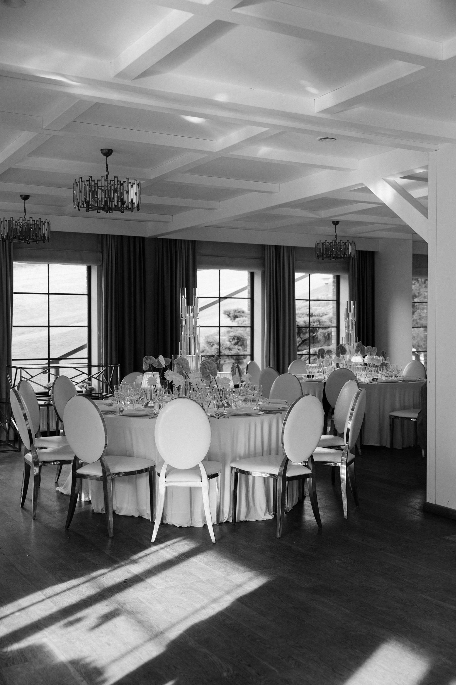 Elegant black and white wedding reception hall with round tables, oval chairs, coffered ceiling and crystal chandeliers.