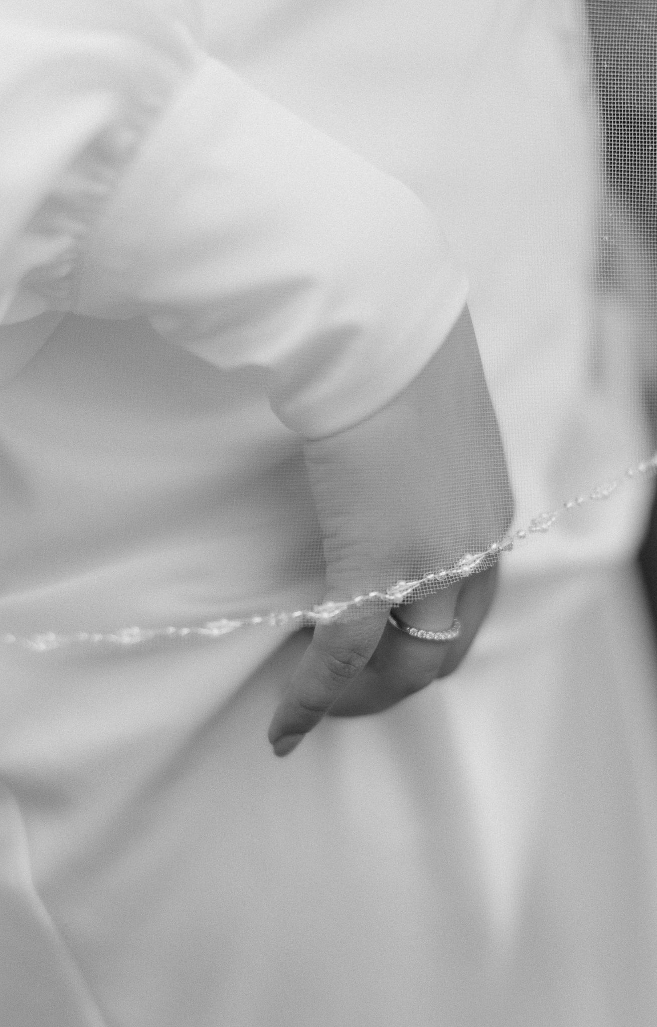Close-up black and white photo of a delicate beaded bracelet on a hand against a white dress sleeve.